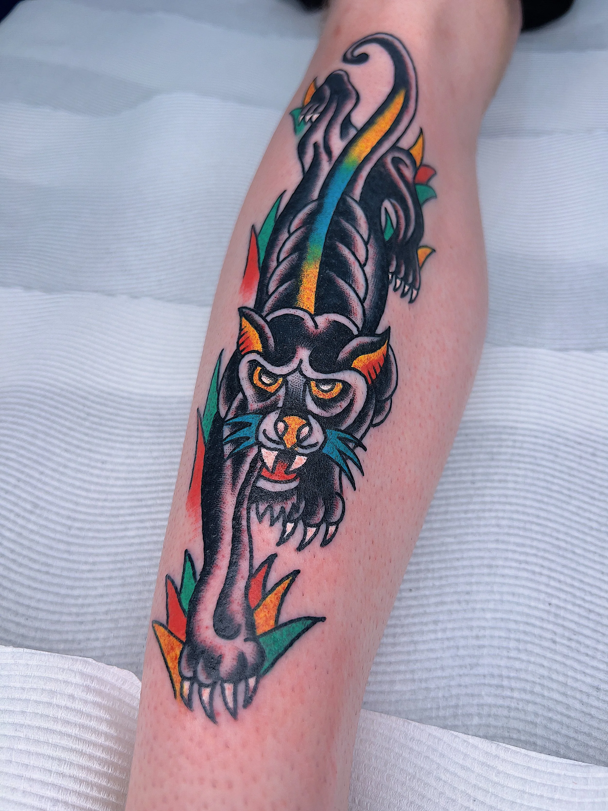 Colorful tattoo of a panther with rainbow stripes on its back and rainbow-colored eyes on a person's arm.