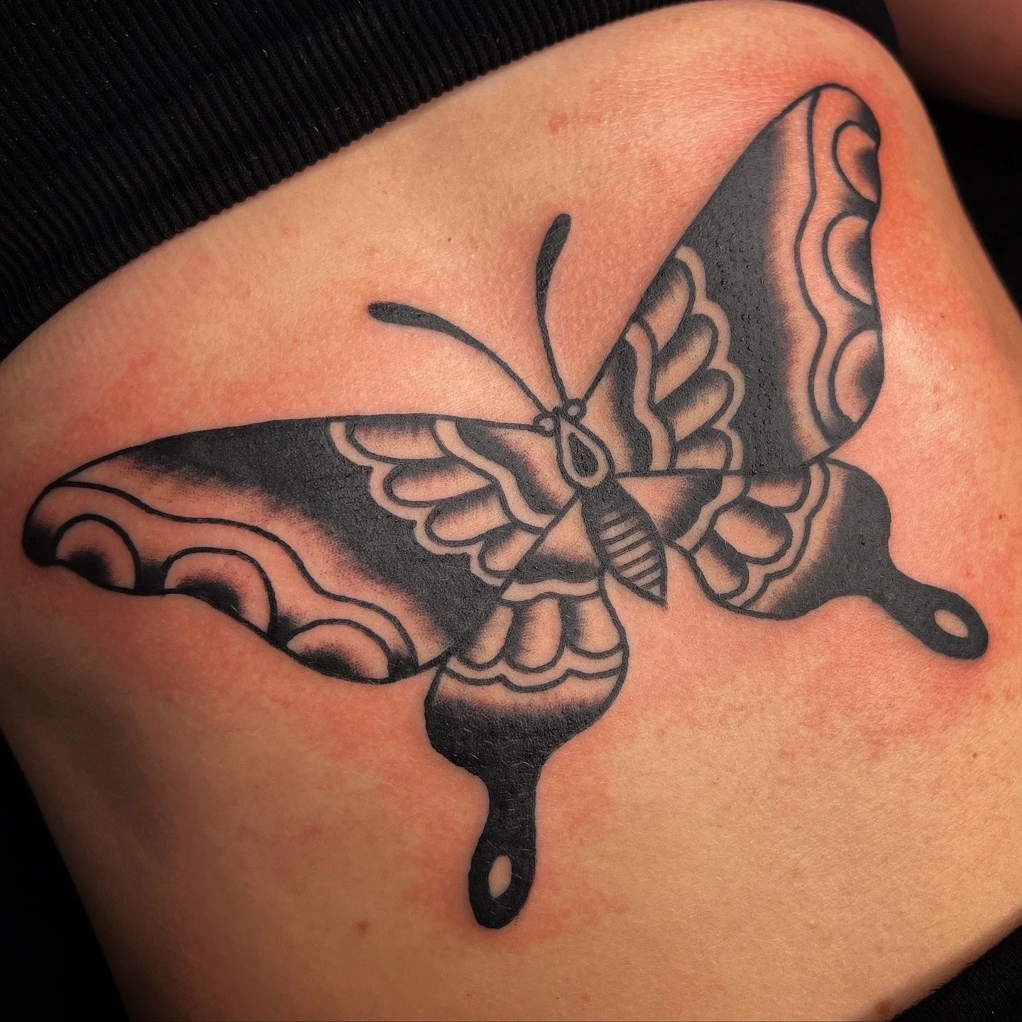 Tattoo of a butterfly with black and gray shading on skin.