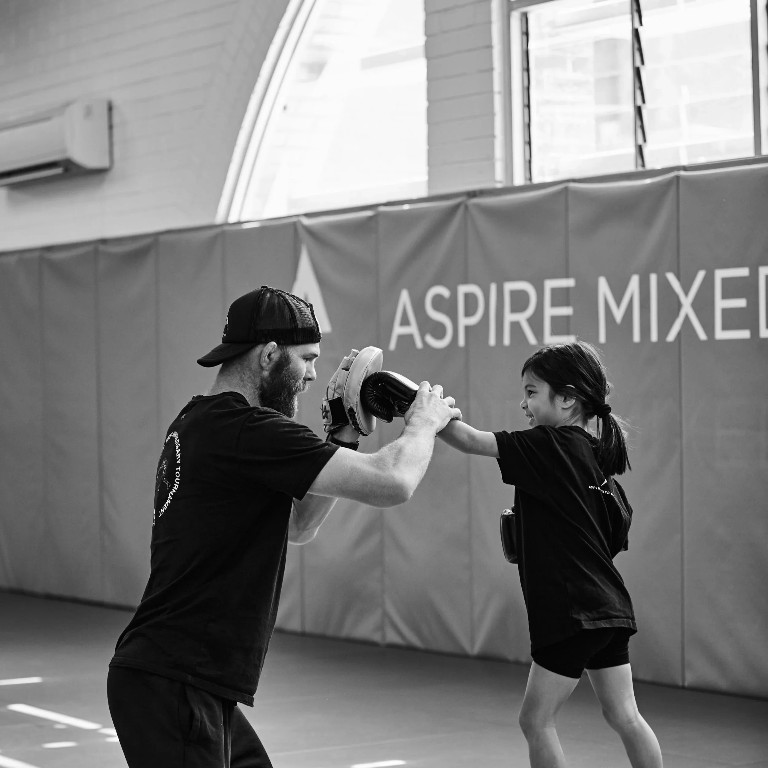 A man and young girl training at Aspire MMA gym, exchanging a high-five. Kids self-defence, boxing, MMA, UFC, boxing, BJJ, grappling, jiu jitsu, wrestling, self-defence, kick boxing, fitness, community. little legends class
