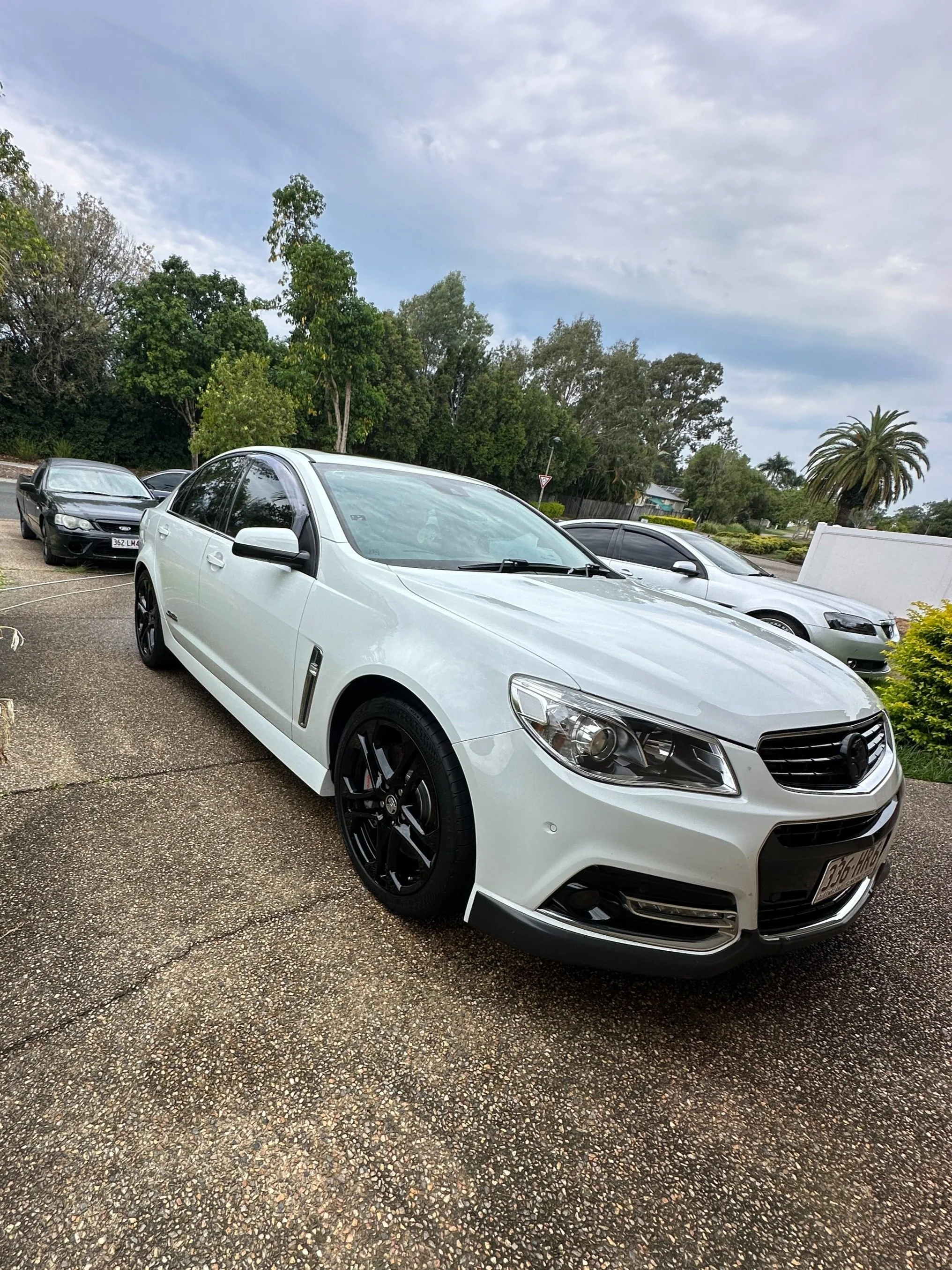 Detailed white sedan parked on a driveway, highlighting a pristine exterior finish after Steam & Gleam’s mobile car detailing service