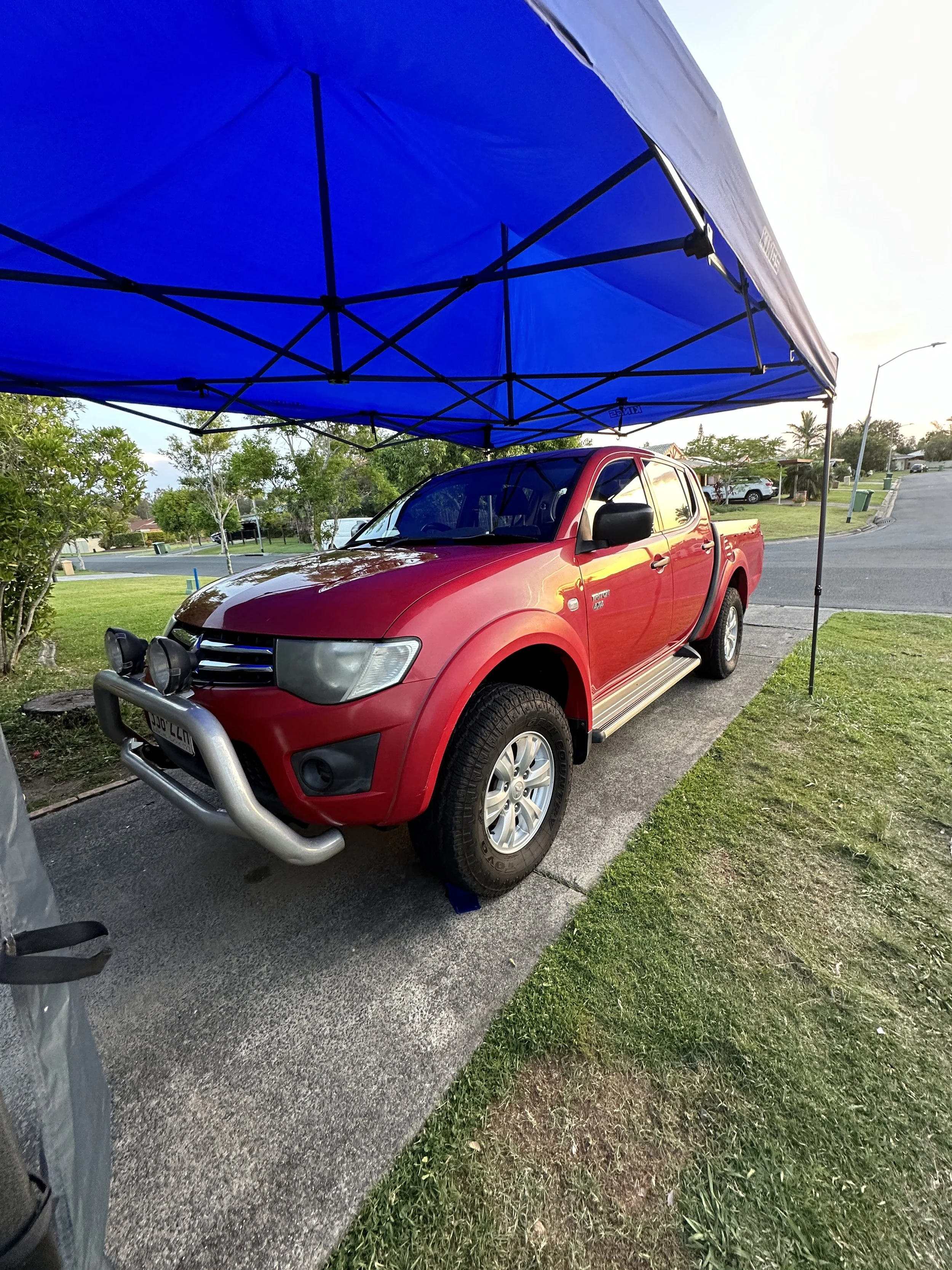 Red pickup truck under a blue canopy, receiving an exterior detail by Steam & Gleam’s mobile detailing team, ensuring a refreshed and polished look