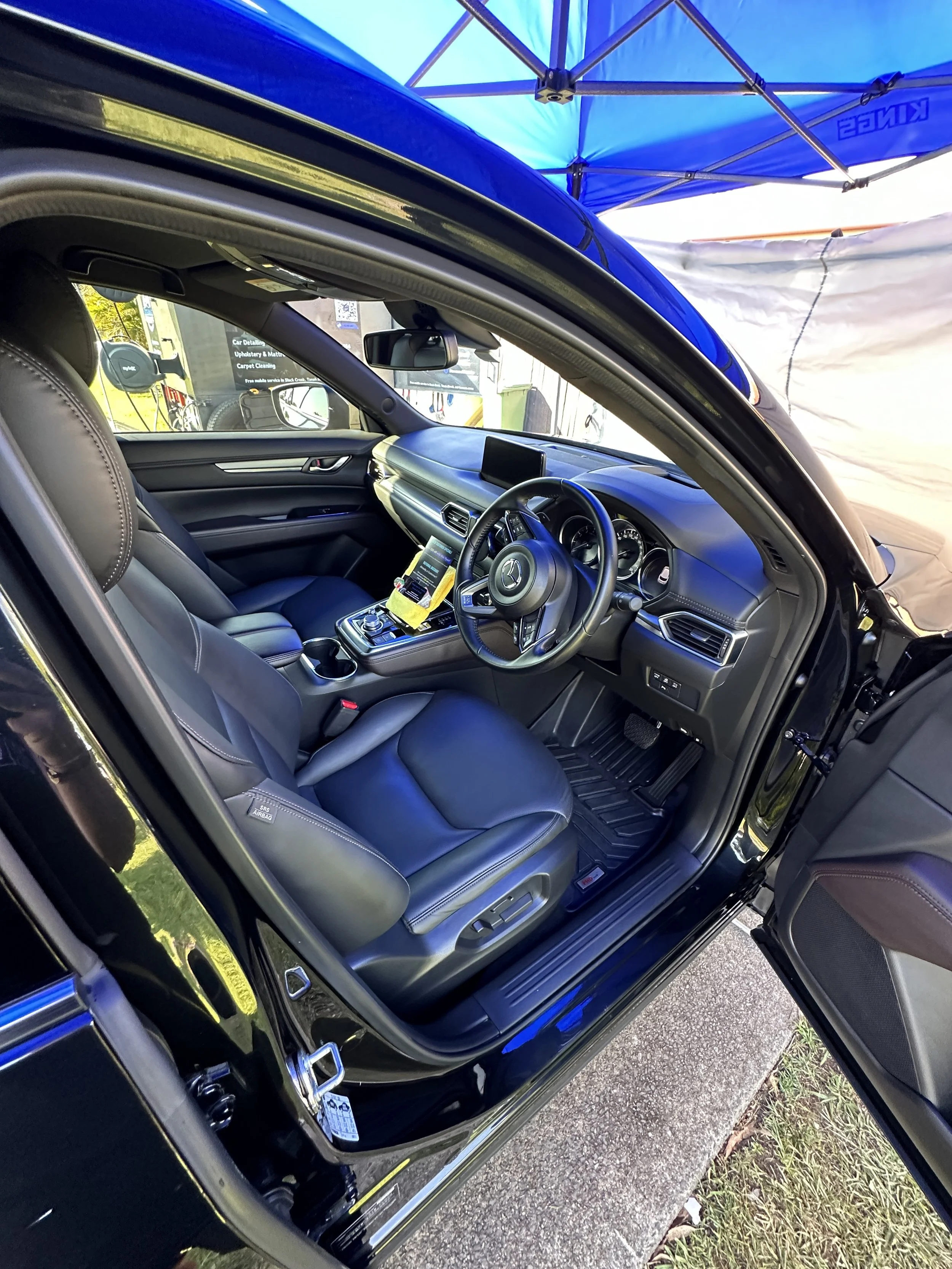 Mazda interior with professional detailing, showcasing pristine seats, dashboard, and door panels under a protective canopy.