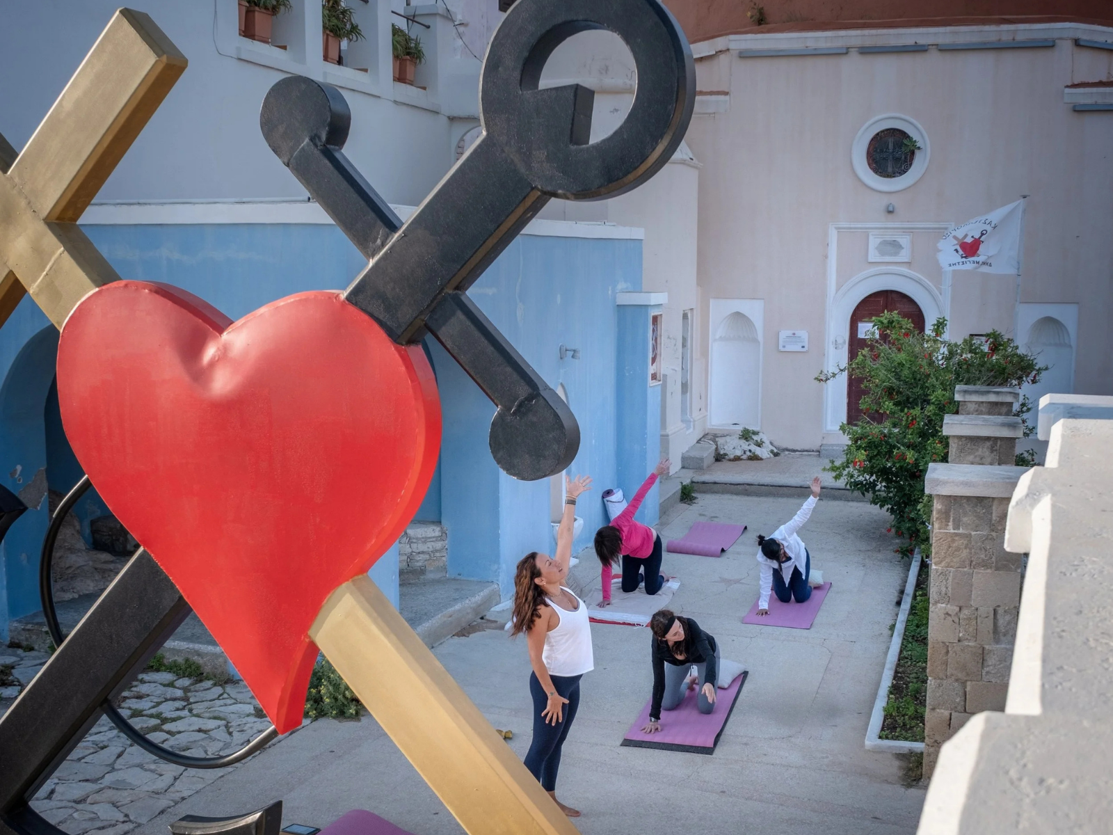People practicing yoga outdoors, with a large decorative heart and arrow sculpture in the foreground