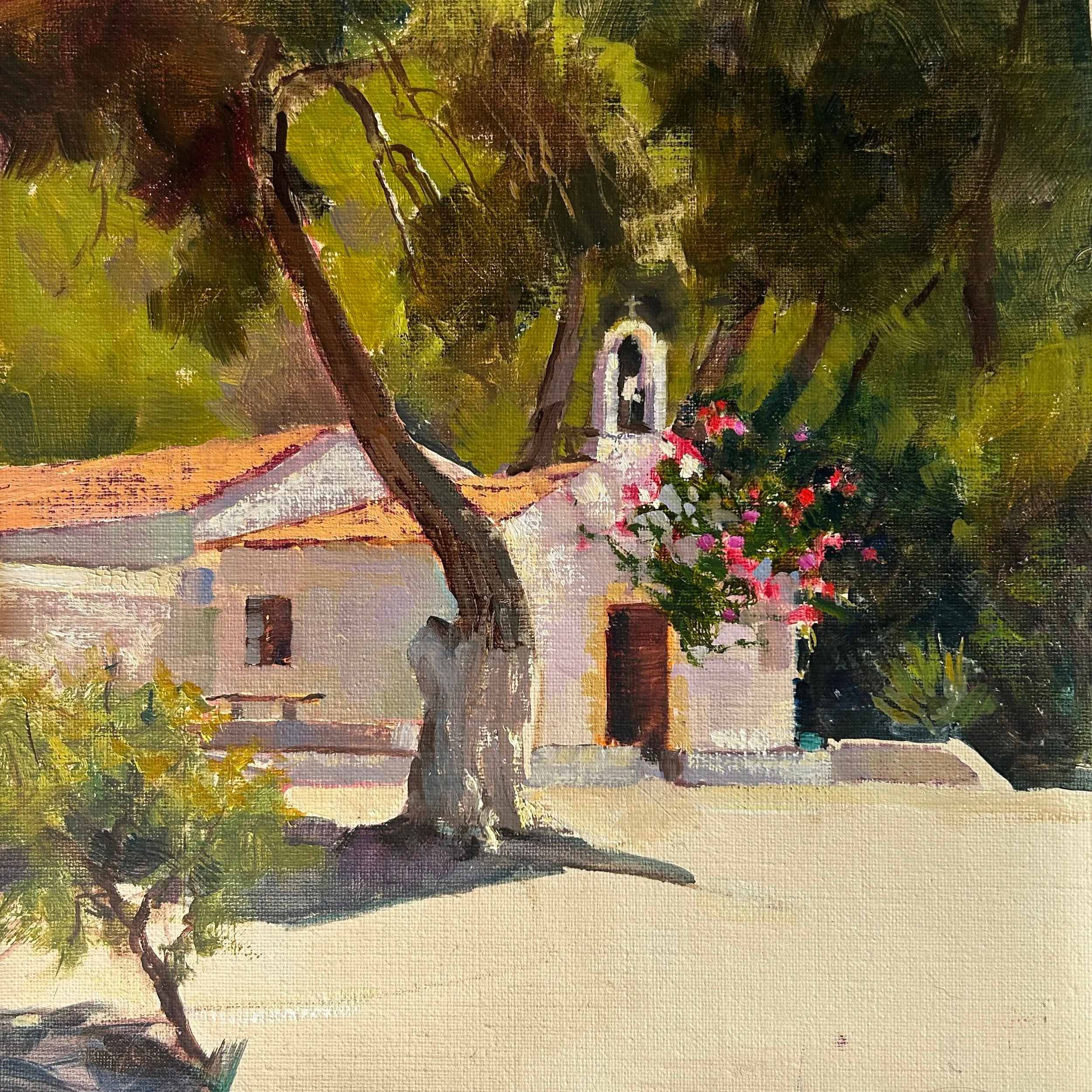A small white church with a bell tower, surrounded by trees and pink flowers, under a green leafy canopy.