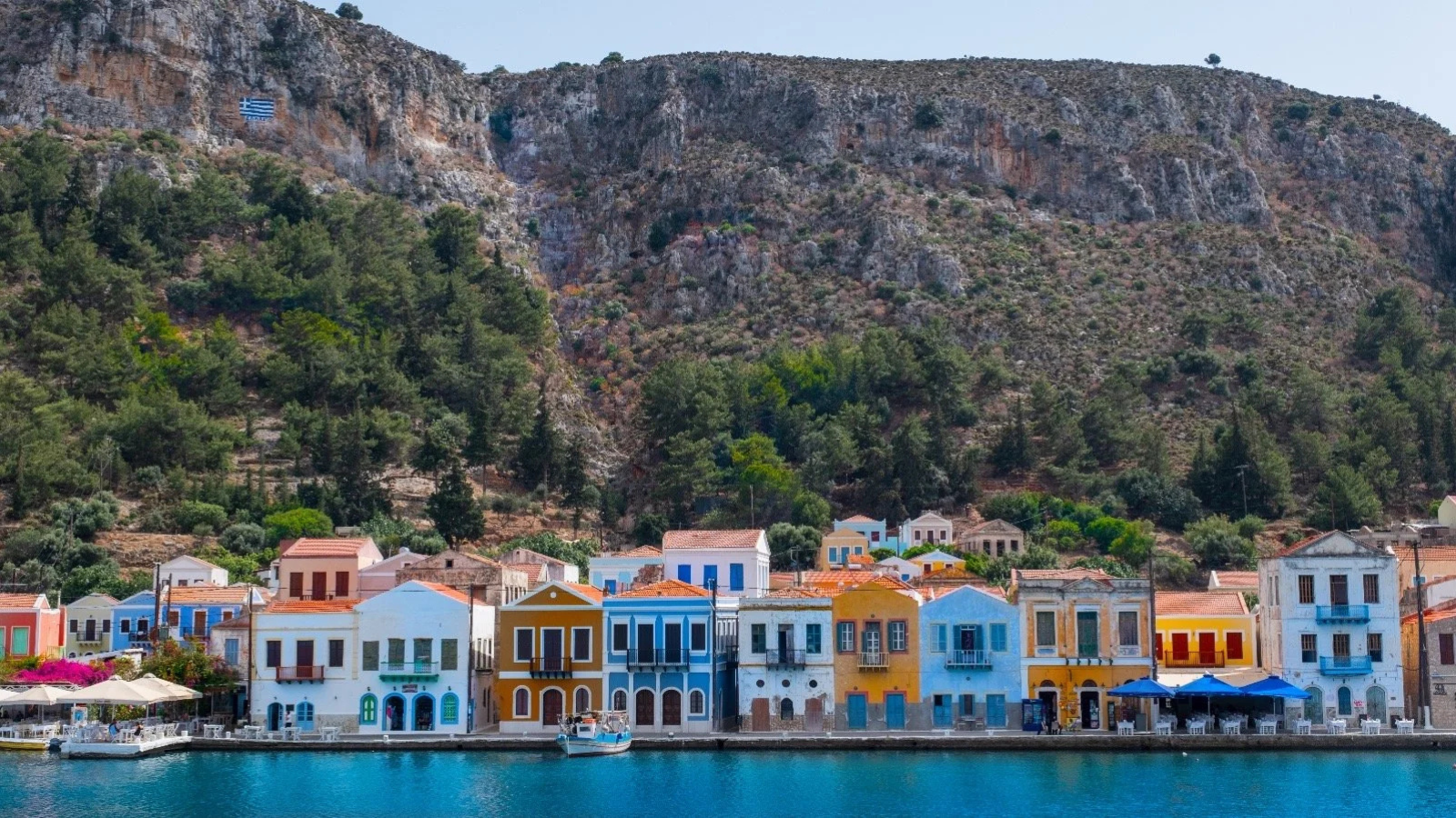 Colorful houses along a waterfront with a mountain covered in trees in the background.