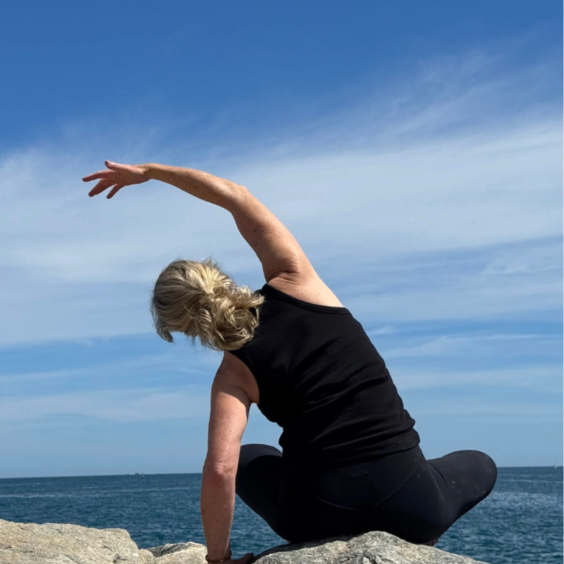 Woman practicing pilates stretches on rock overlooking greek ocean