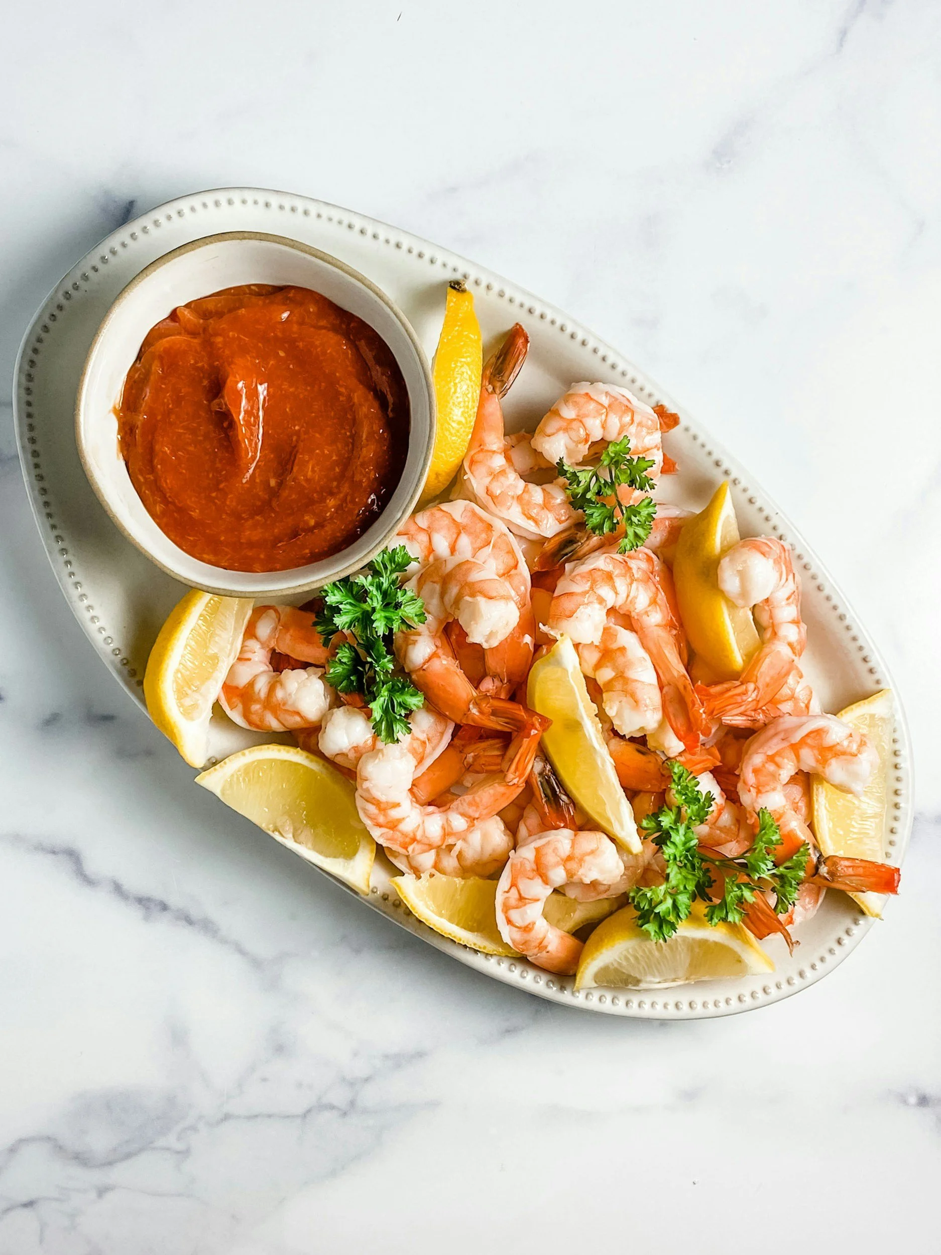 Platter of chilled Gulf shrimp with tangy cocktail sauce and lemon wedges, a New Orleans remoulade-style presentation