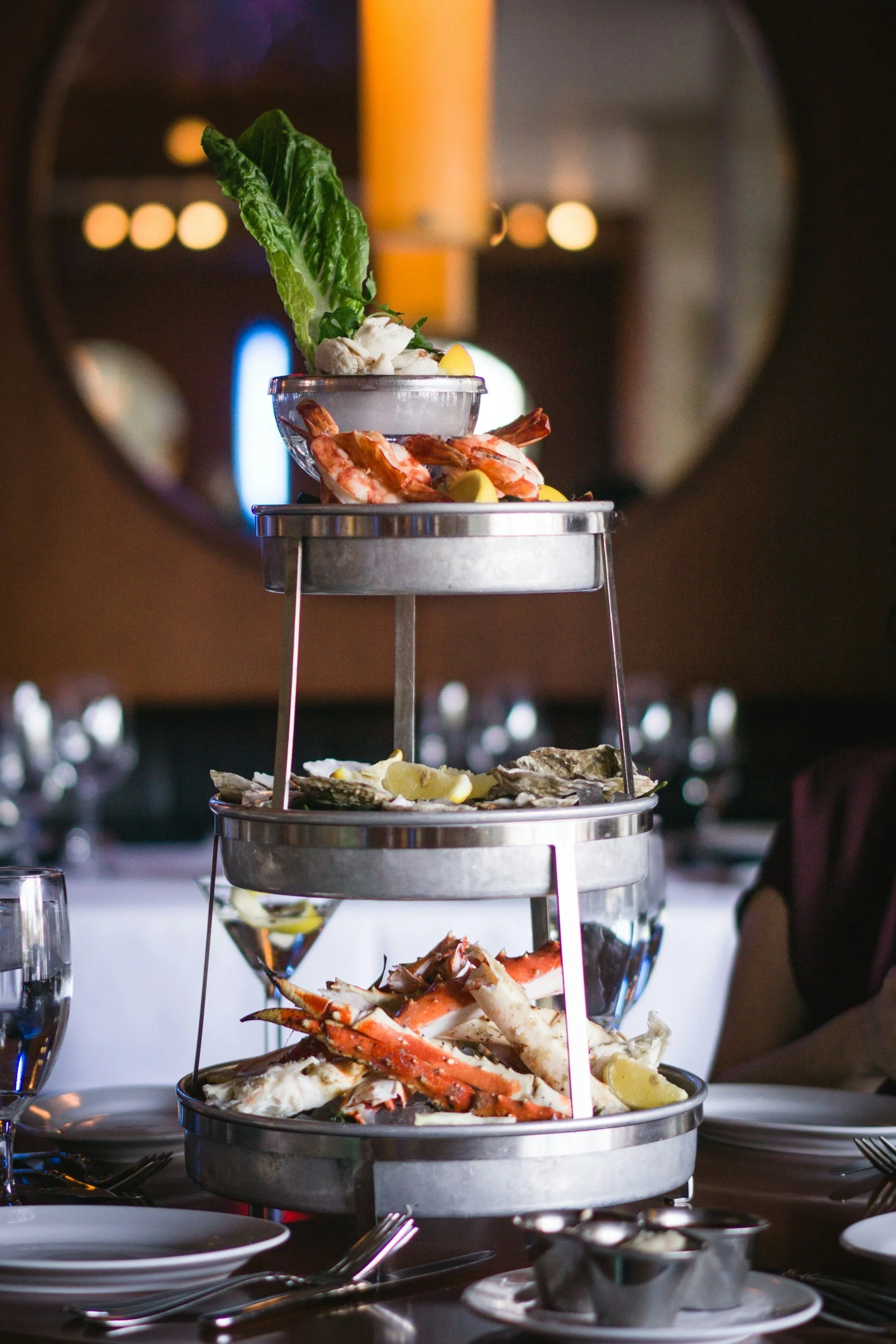 A three-tier seafood tower elegantly presented at a restaurant table, an example of a labeled, tiered raw bar display