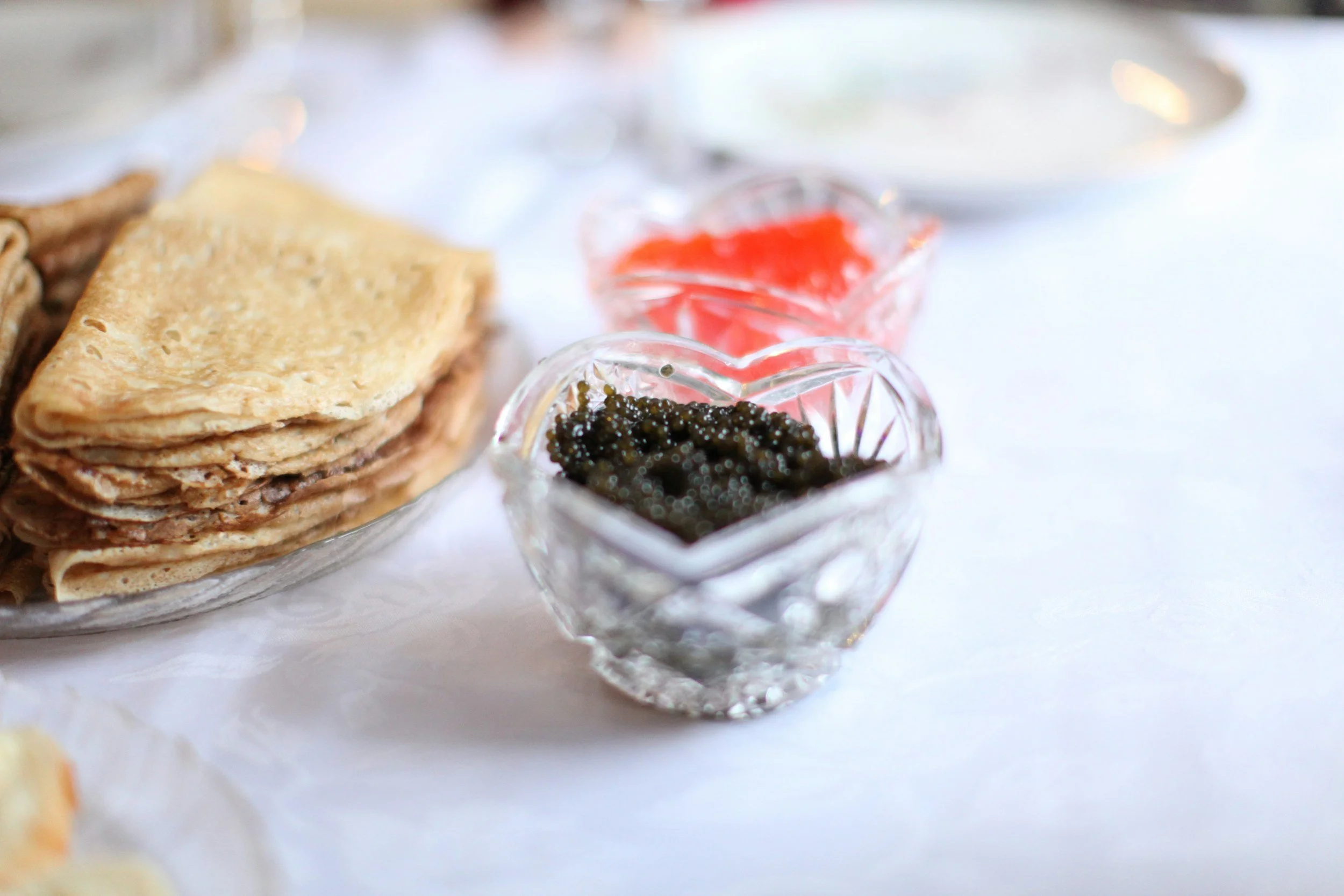 A Small bowl of black caviar next to crepes