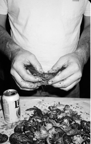 a man in a white shirt with a beer peeling crawfish