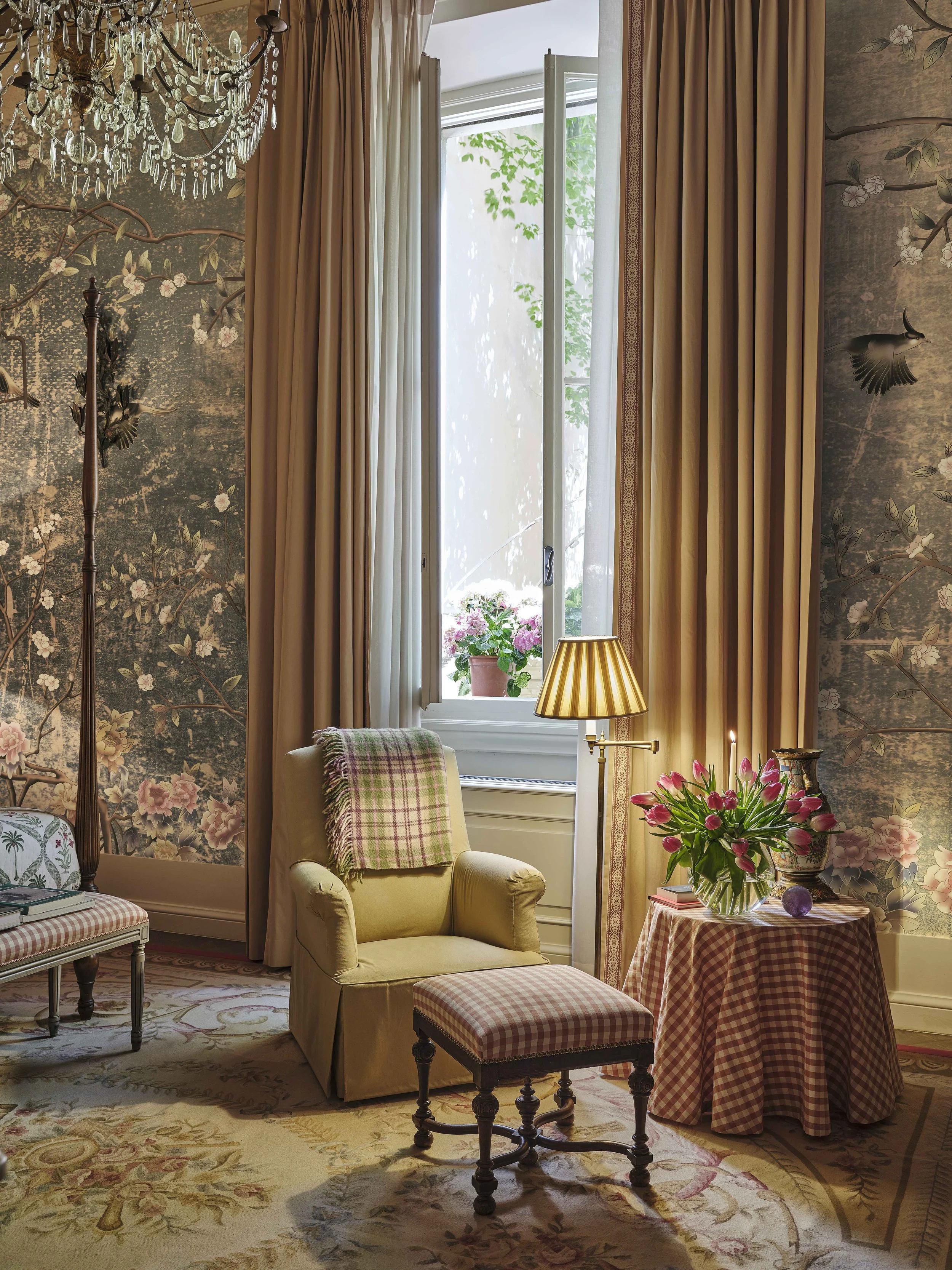 Chinoiserie bedroom seating area with scenic wallcovering, tailored curtains, a slipcovered armchair and layered patterned fabrics patterns and weaves