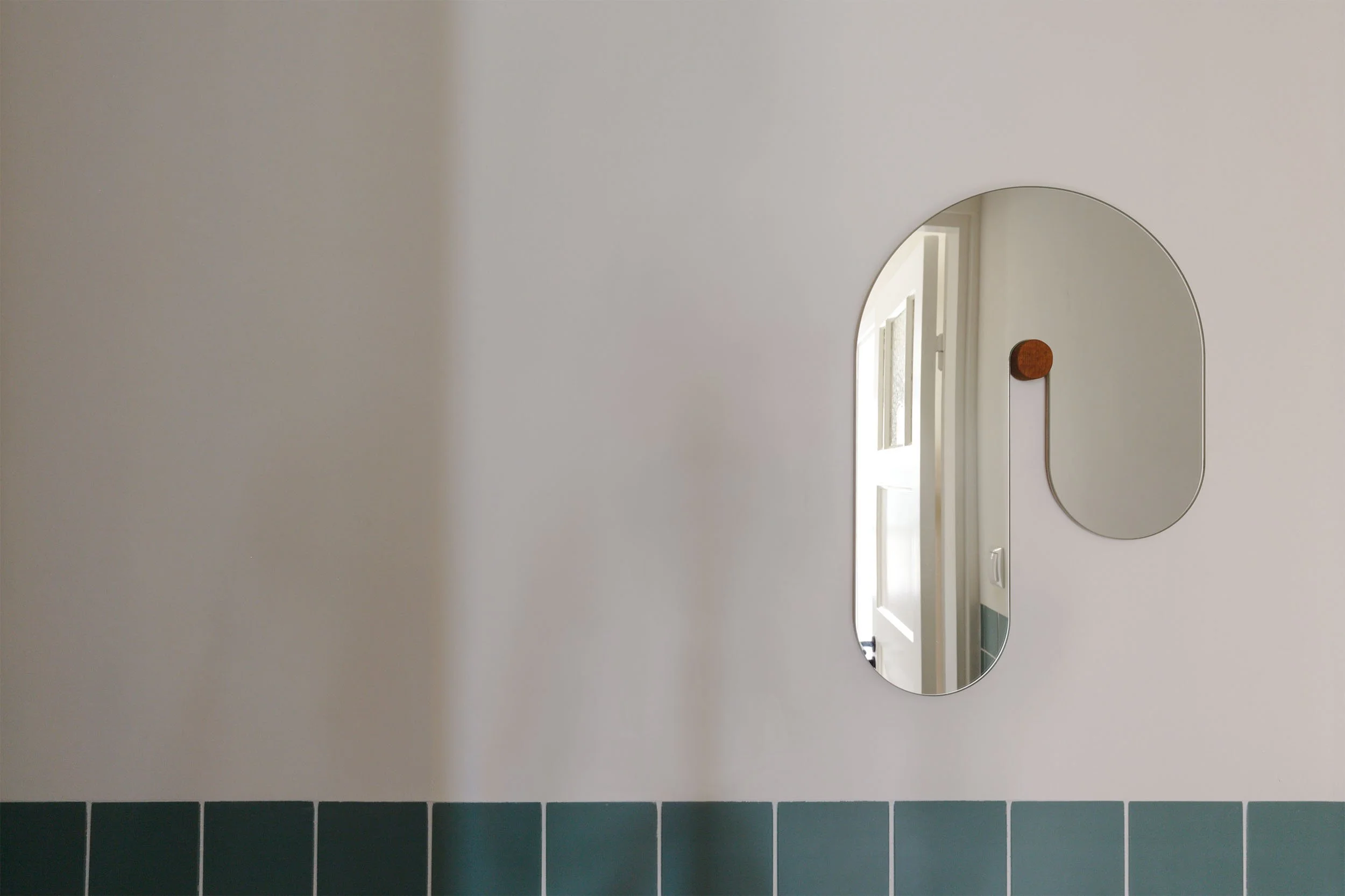 Gebogen spiegel op eikenhouten knop in badkamer met groene tegels