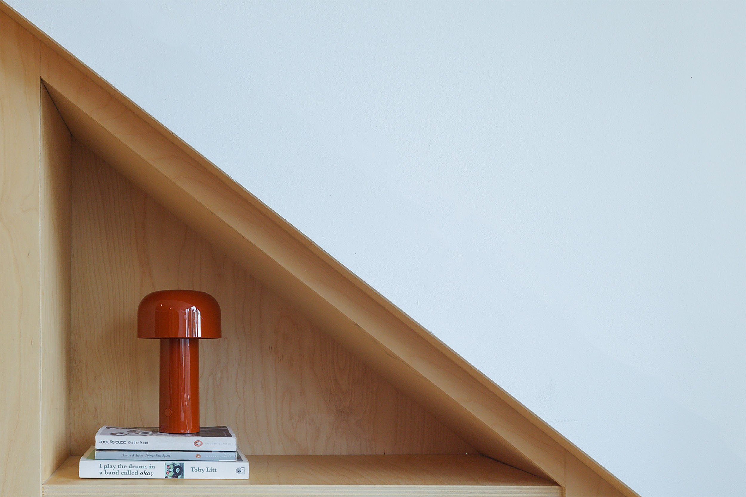 Flos Bellhop lamp op boeken in berken multiplex kast onder schuin dak