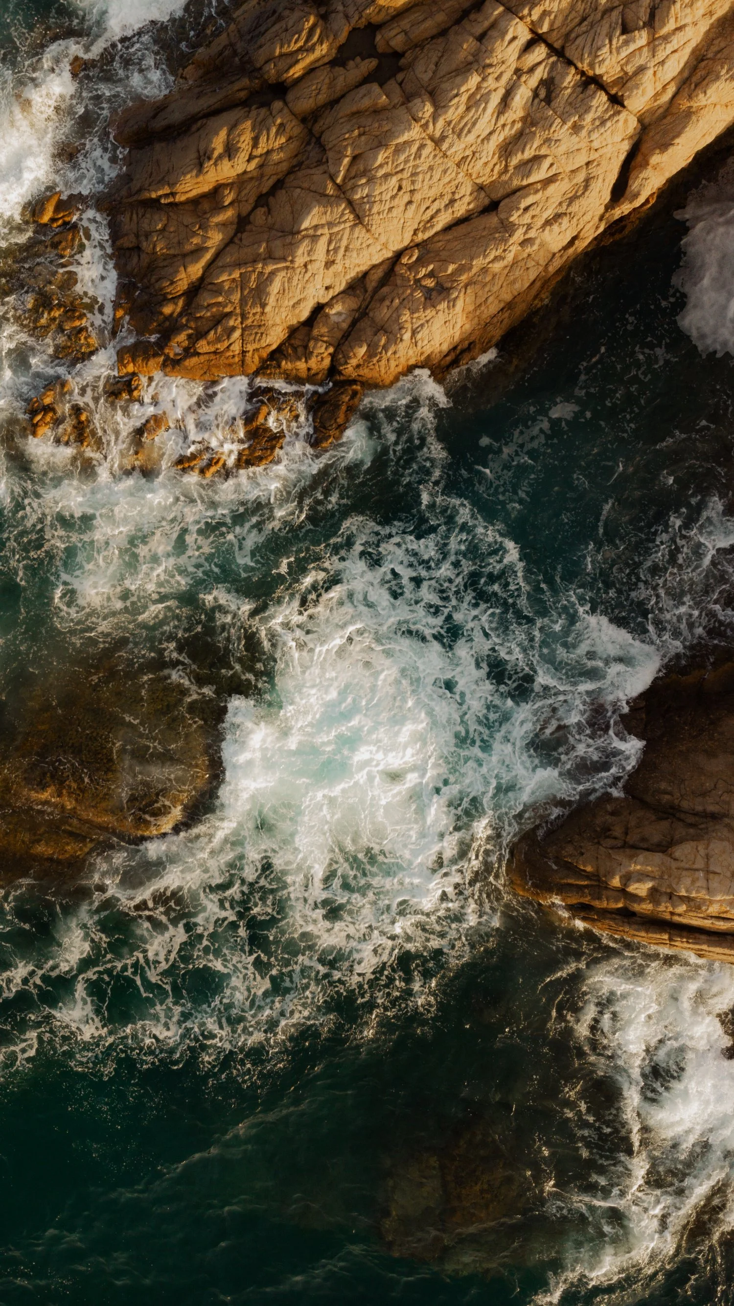 Vista aérea de olas rompiendo contra rocas en el océano.