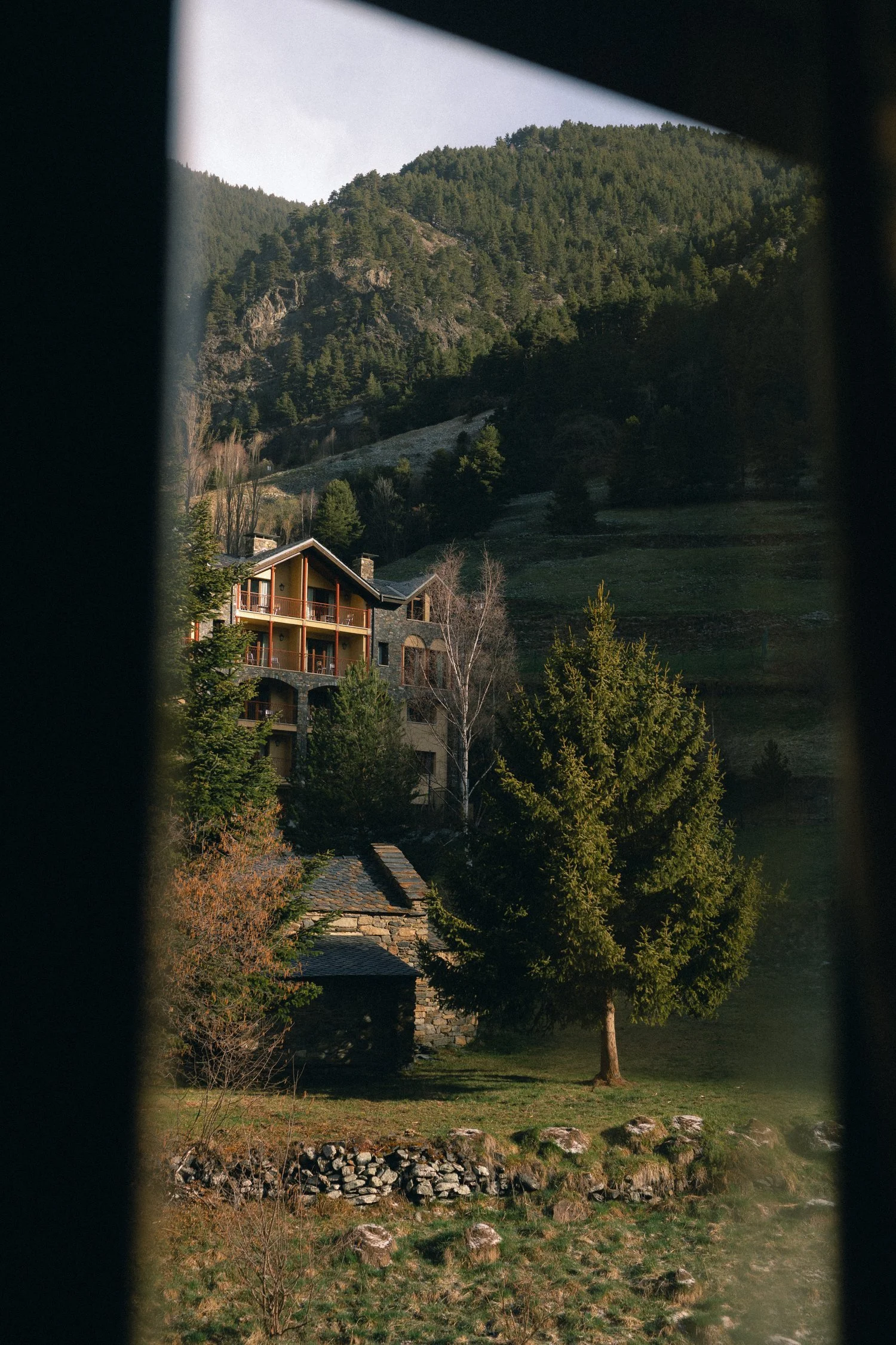 Vista de una casa de montaña rodeada de árboles y naturaleza, vista a través de una ventana o ventilación.