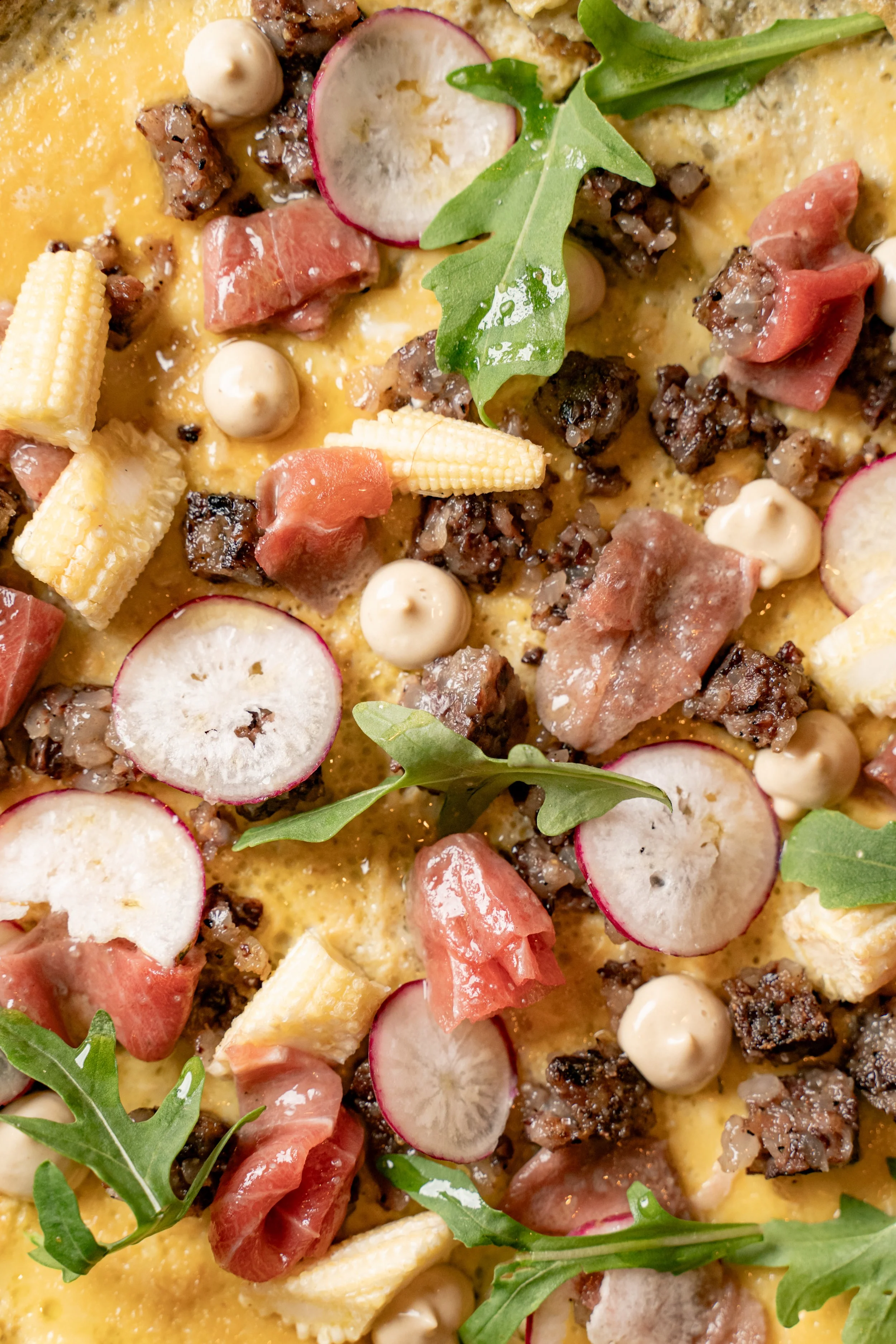 Una pizza con queso, tocino, rodajas de rábano, hojas de rúcula y pequeños cubos de pollo.