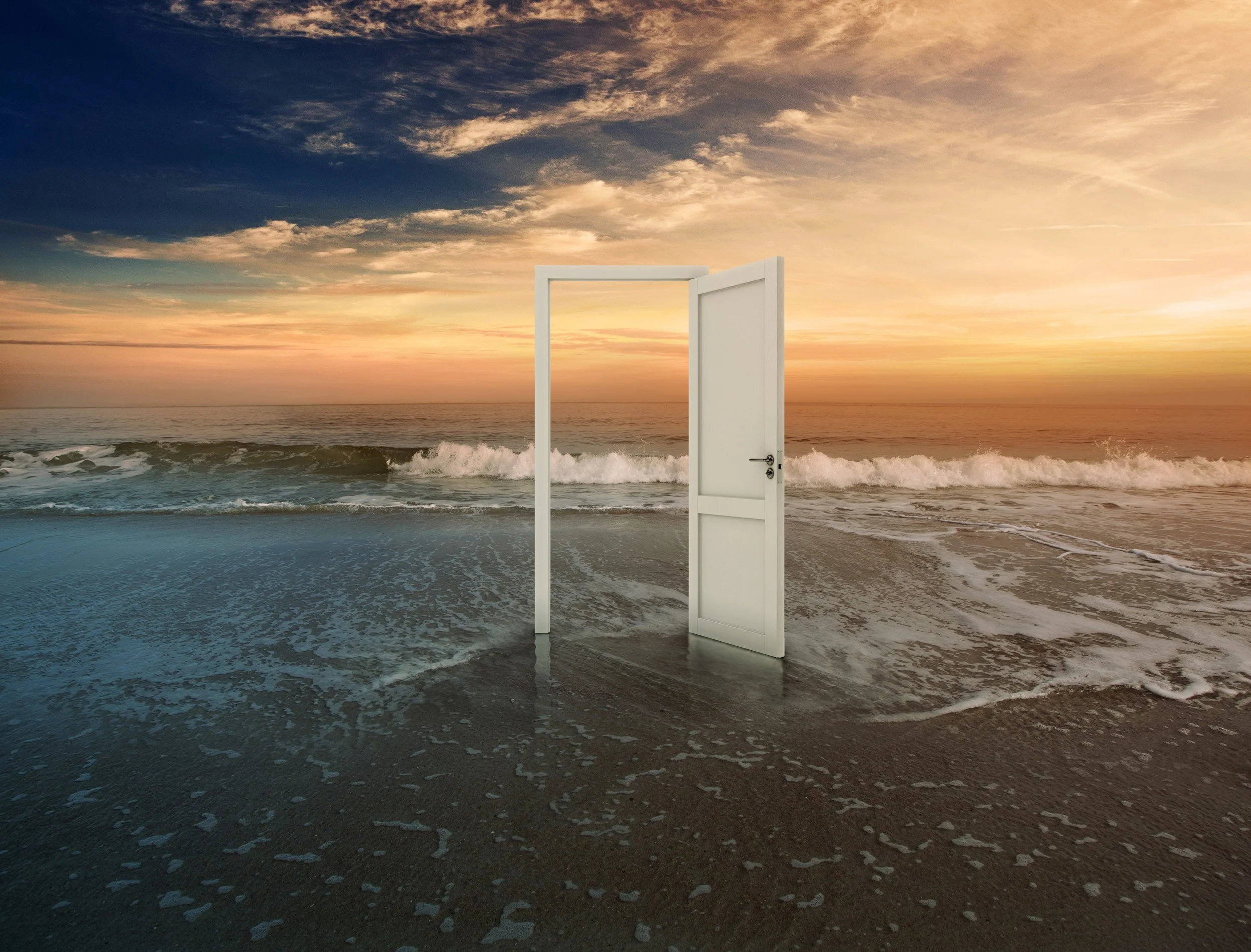 A white door standing open on a beach, with the ocean waves and a colorful sunset sky in the background.