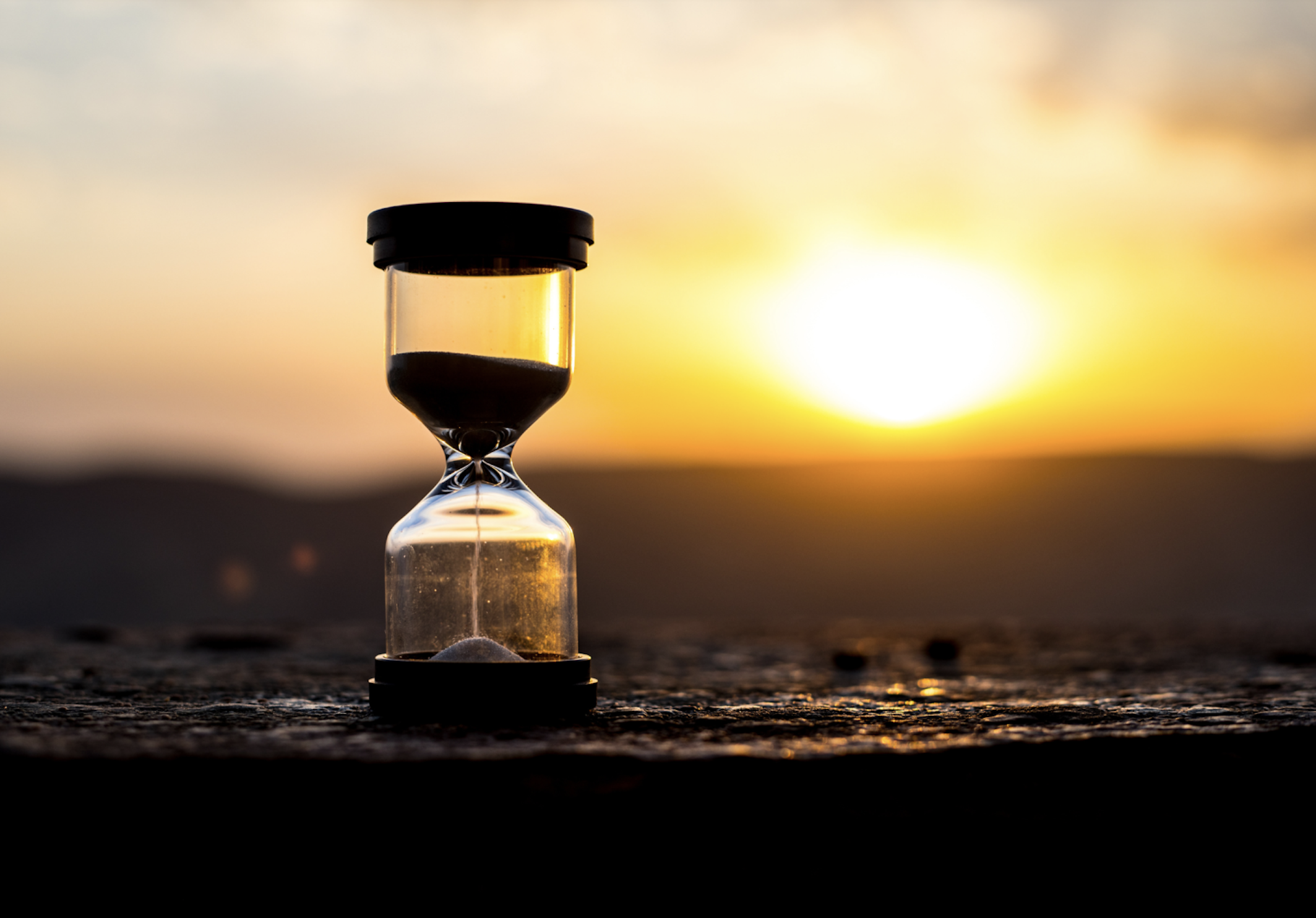 A small glass vial with black cap containing dark substance, placed on a textured surface, with a sunset or sunrise in the background.
