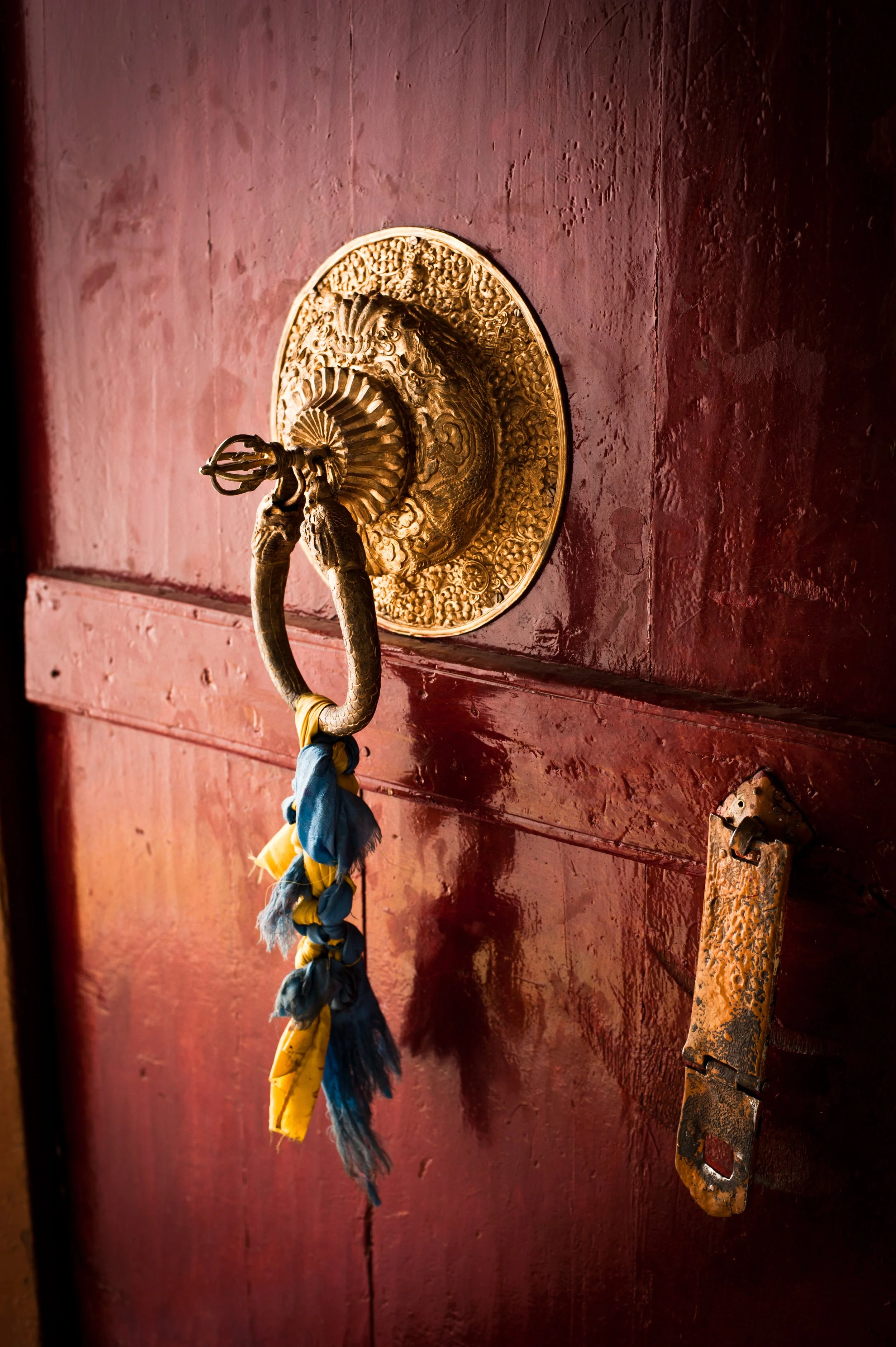 An ornate gold doorbell with a decorative surround and a braided fabric rope hanging from it, mounted on a red painted door.