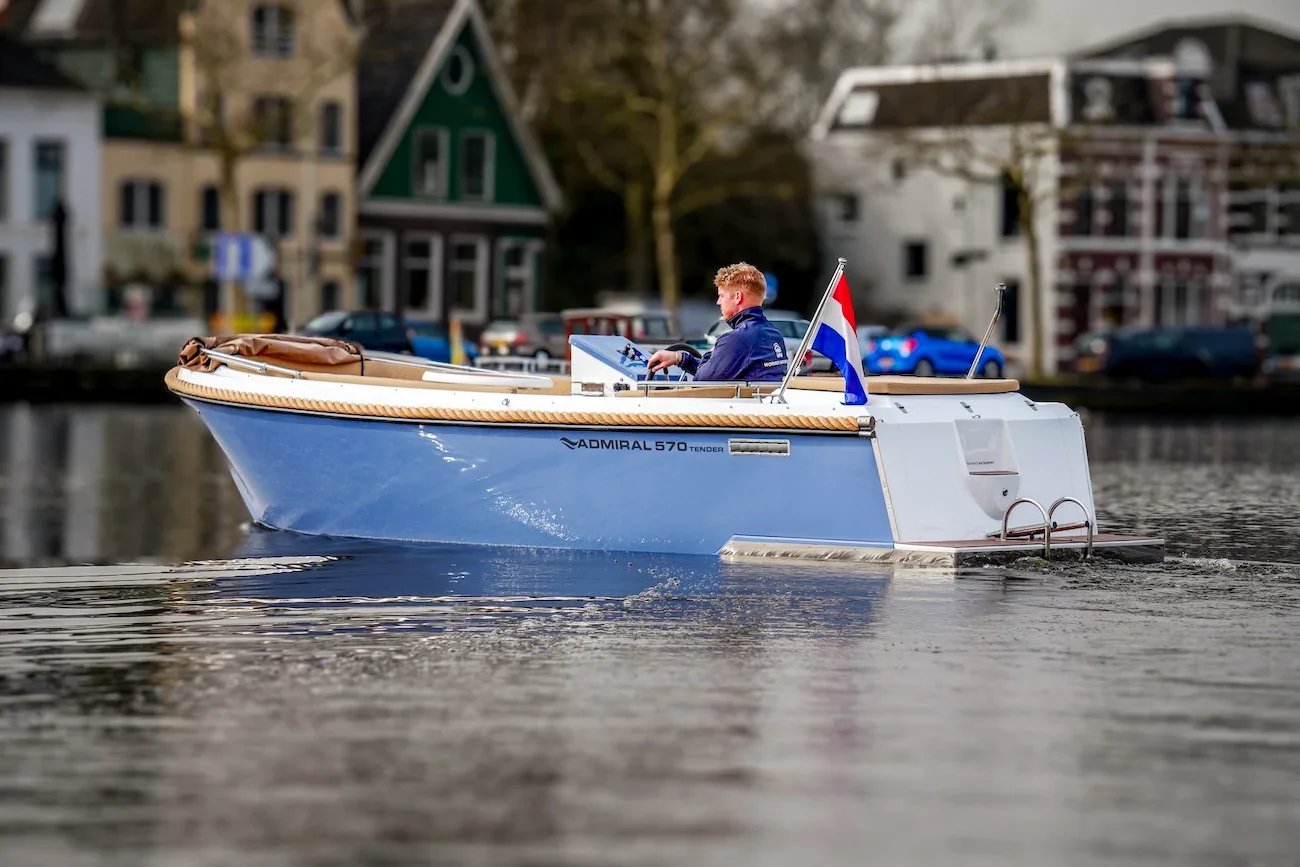 een oud of lichtblauwe tender sloep met suzuki buitenboordmotor in het water met nederlandse vlaggenstok ergens in noord-holland in de zaanstreek. Wormer. Wormer Watersport sloep kopen boot. 5 a 6 meter