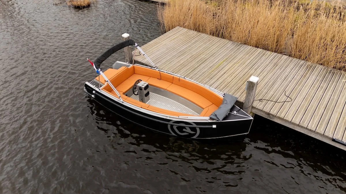 Een aluminium tender boot met oranje bekleding en een grijze romp van Qwest, de S600 op het water aan een steiger aan de zaan van wormer watersport, daar te koop
