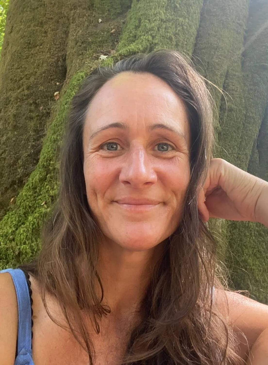 Woman looking straight forward with green mossy tree behind