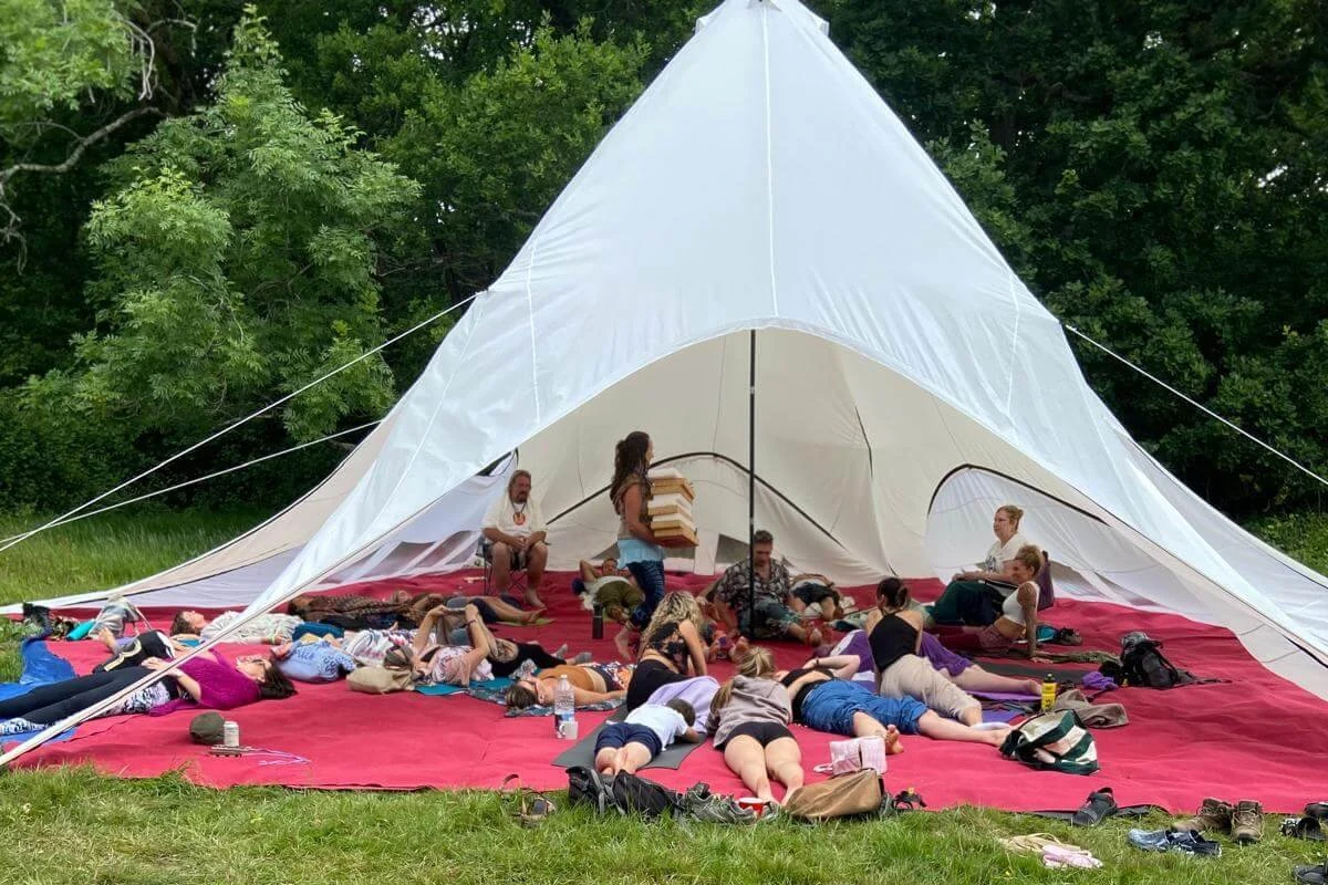 White open tent in a field with red carpet at Freezone Festival with people lying on mats doing yoga