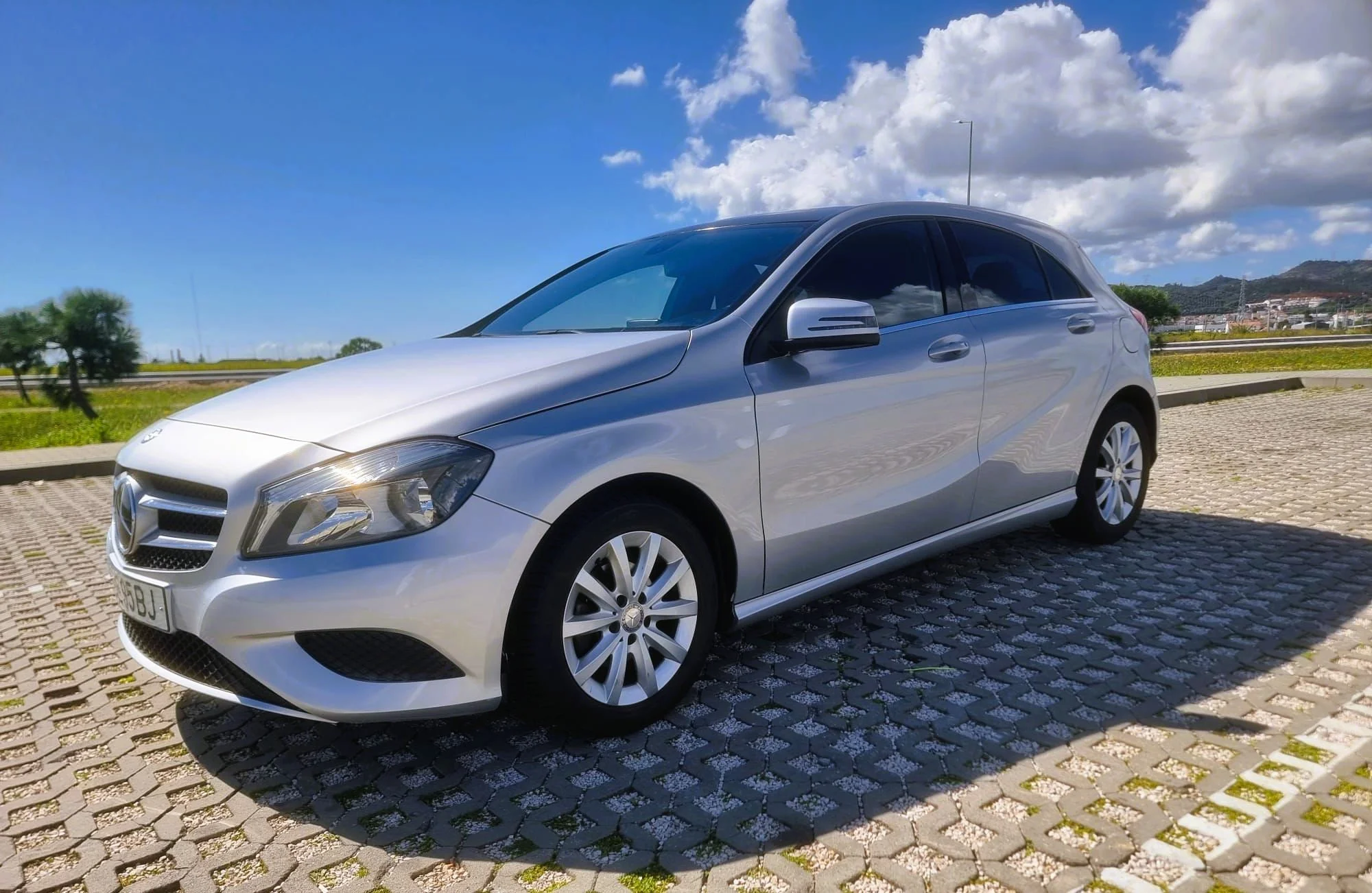 Carro cinza estacionado em um pátio com céu azul e nuvens ao fundo.