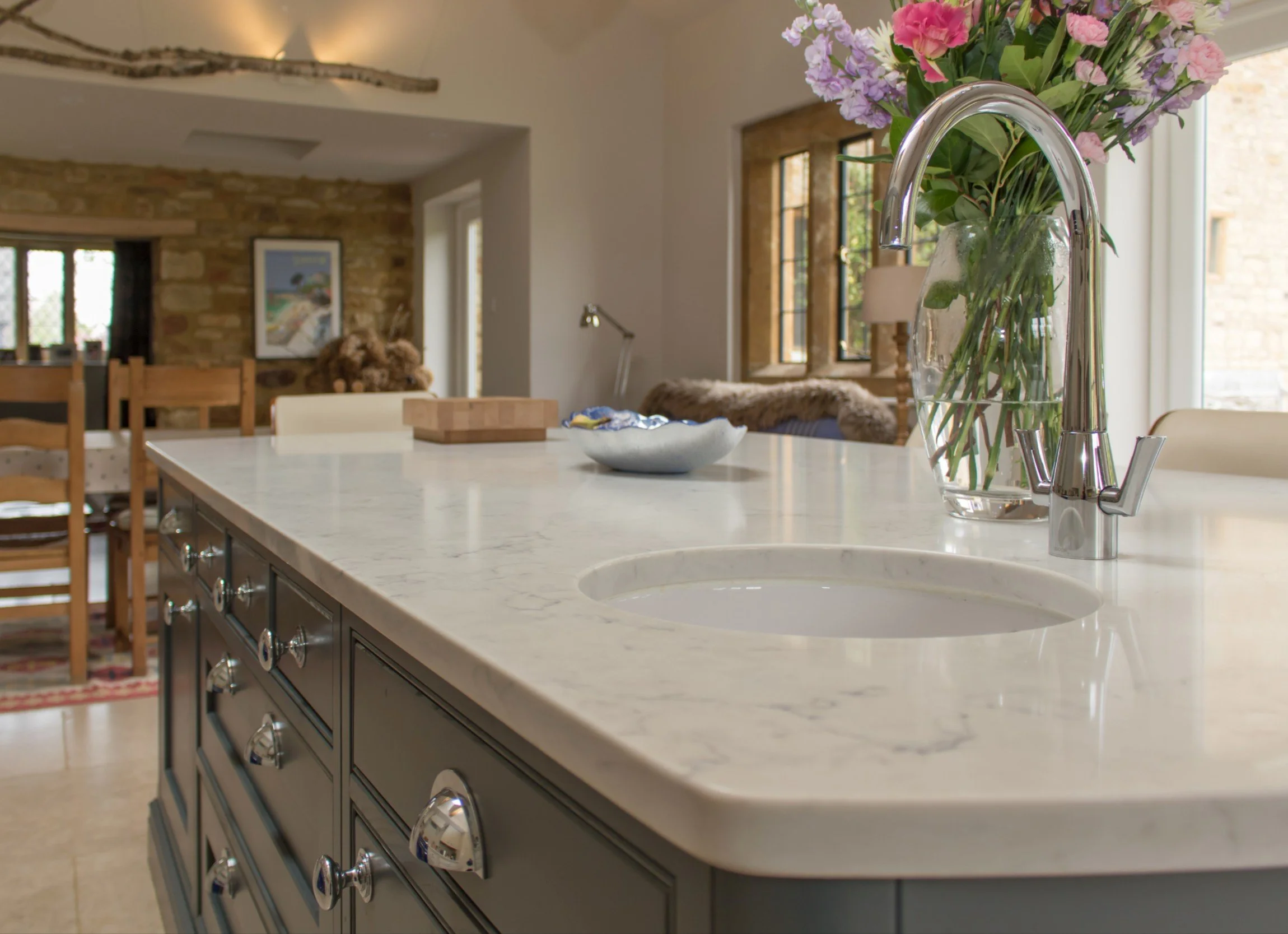 A kitchen with a white marble countertop, a vase with pink and purple flowers, and a stainless steel faucet.