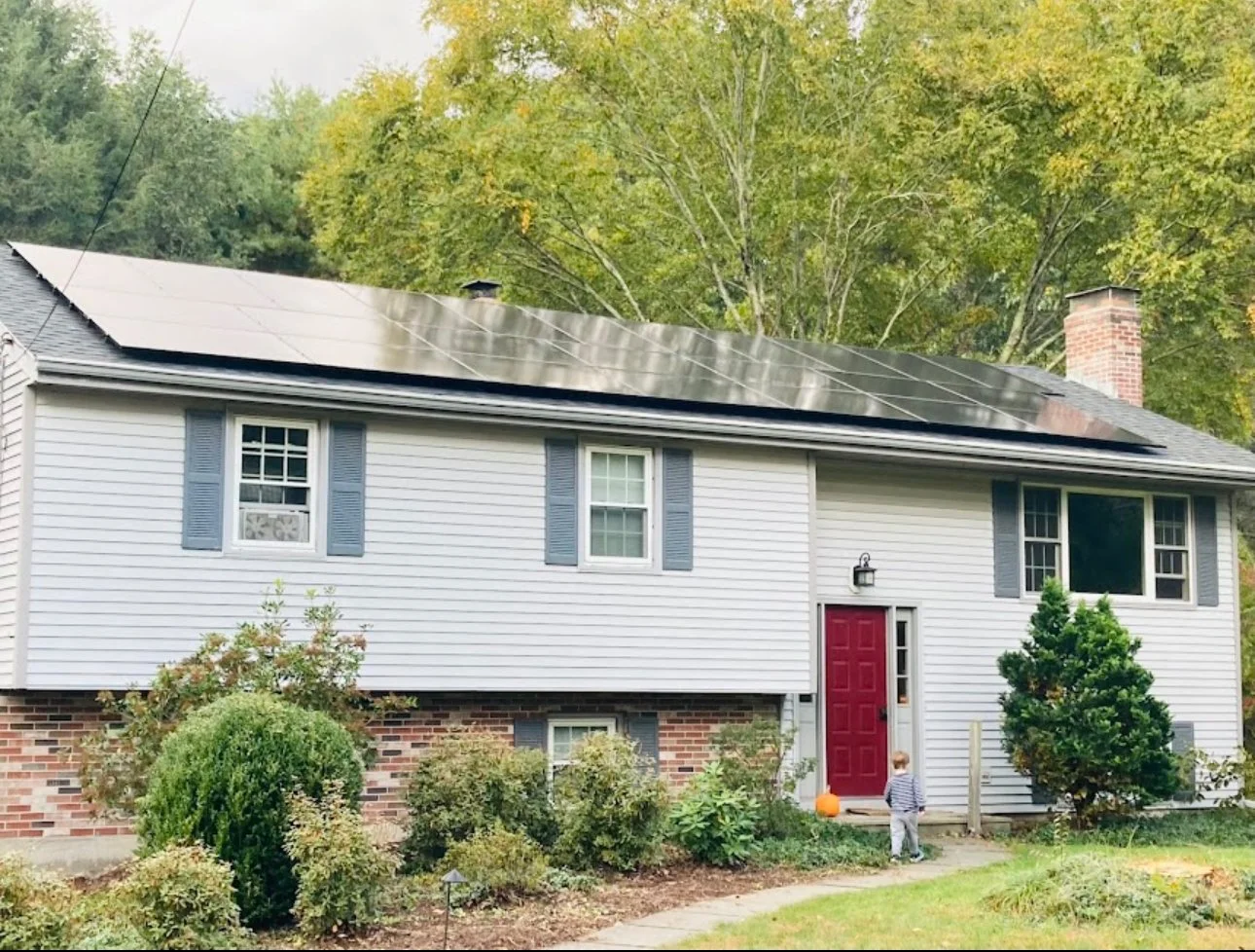 House with solar panels on roof, red front door, and small garden