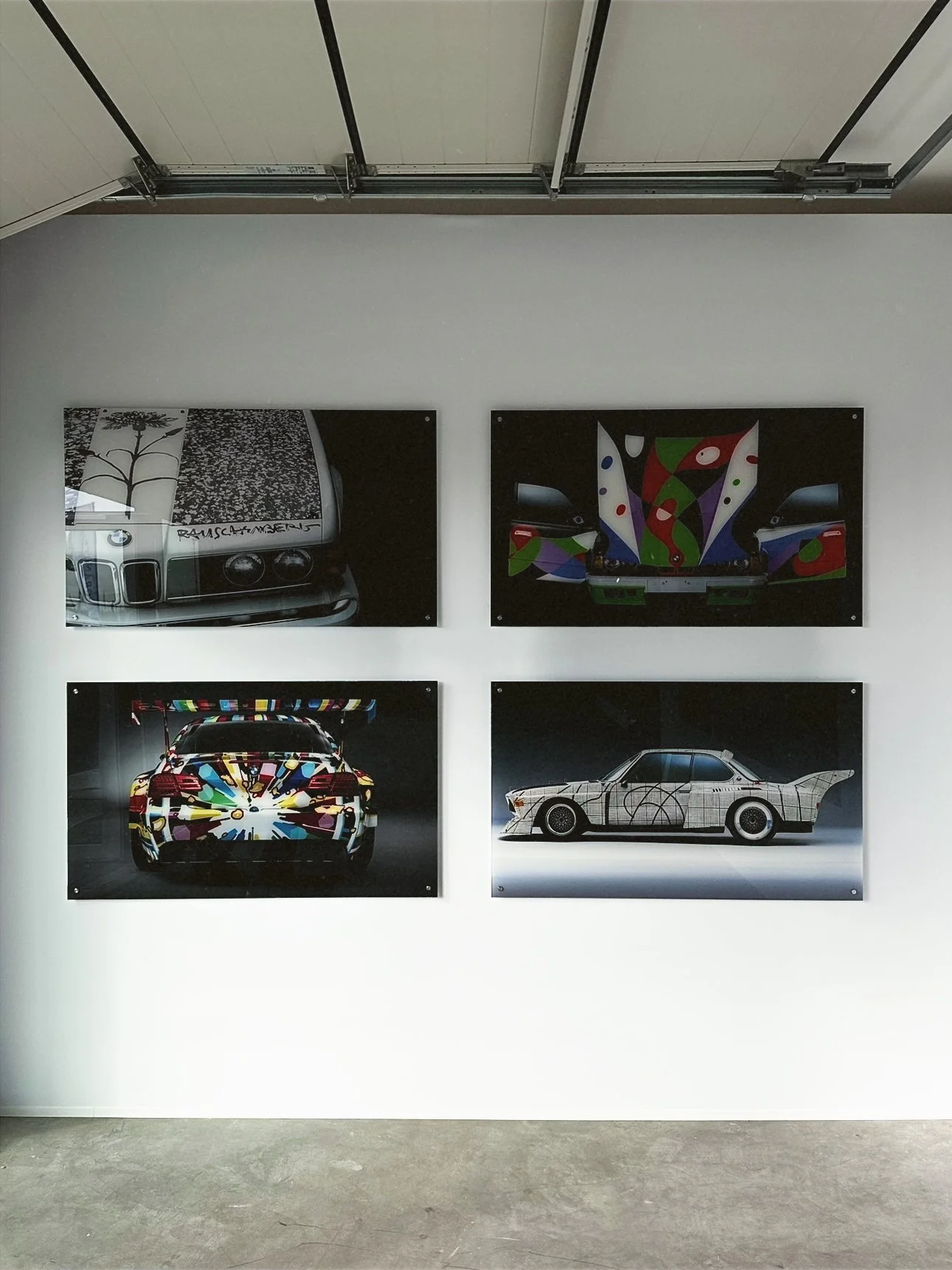 Four art photographs of colorful, stylized cars and abstract designs on a white gallery wall.