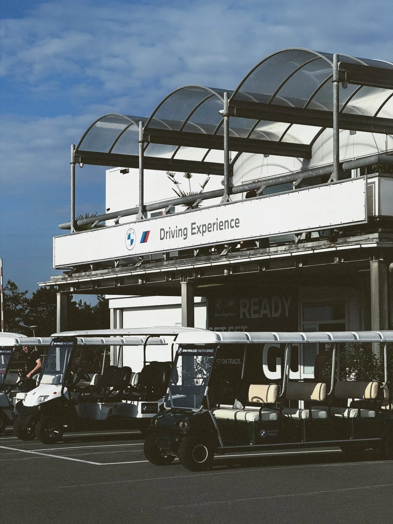 Golf carts parked in front of a building with a sign that reads 'Driving Experience' and the BMW logo.