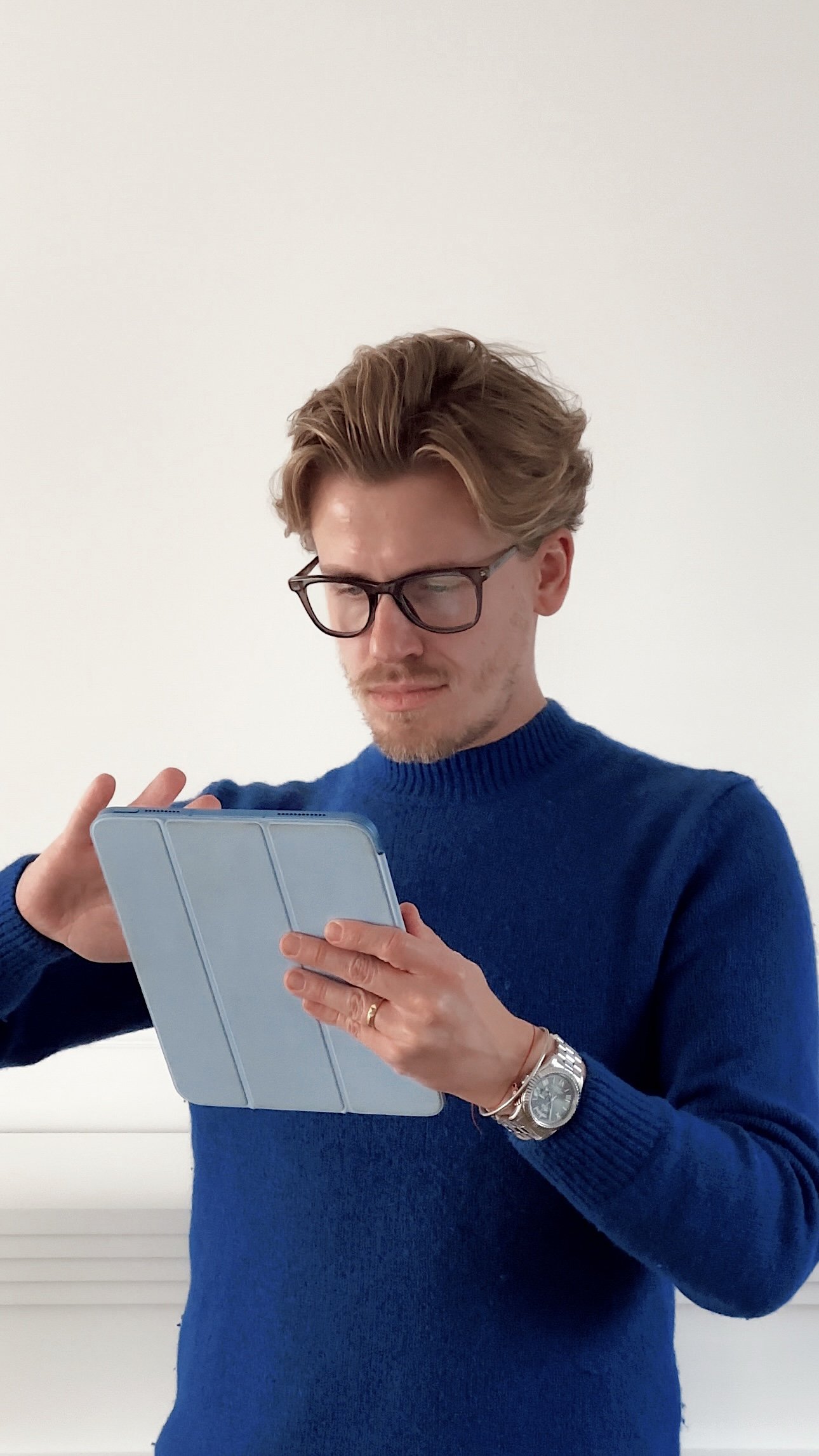 Man in blue sweater and glasses looking at tablet
