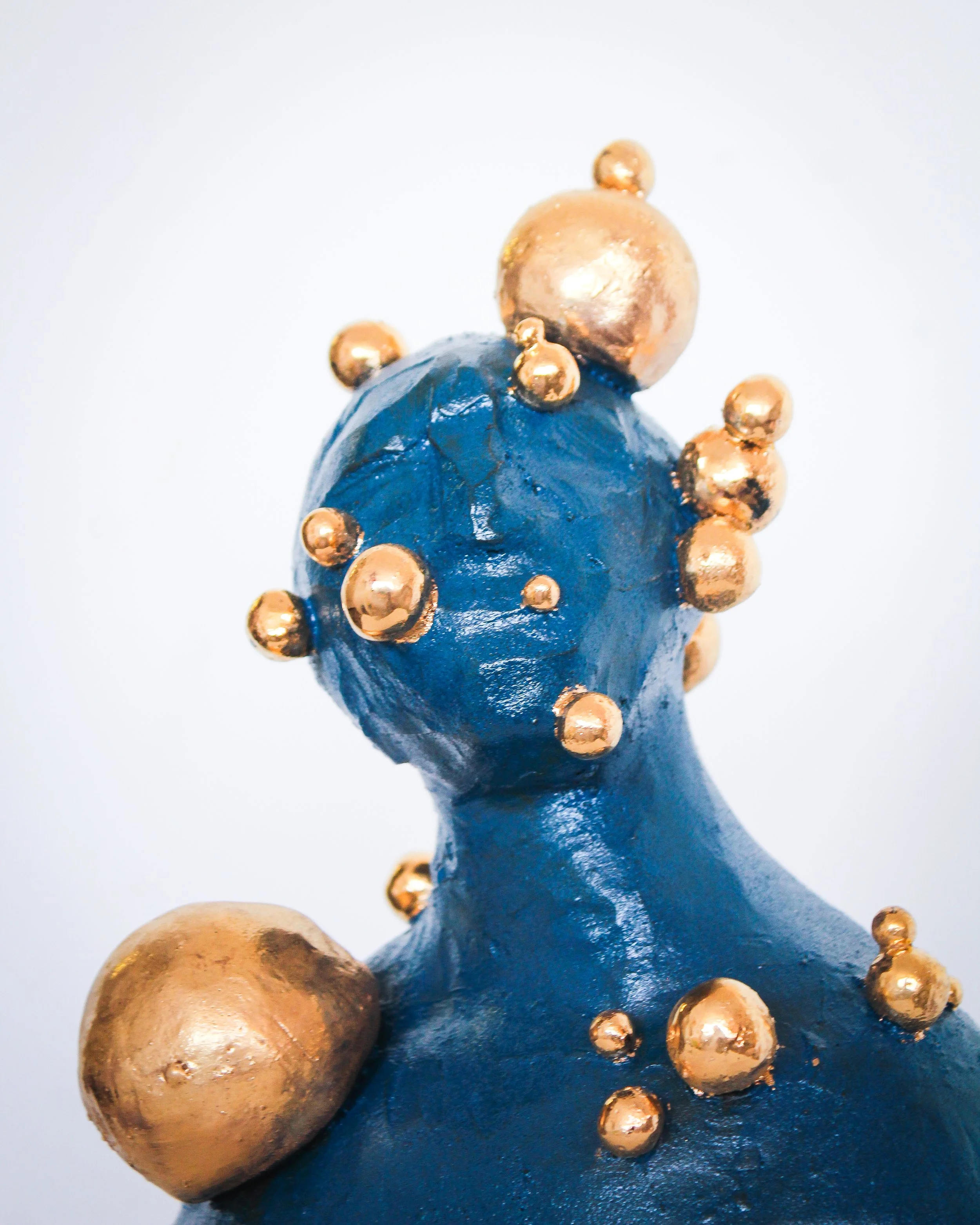 Sculpture of a woman painted in dark blue with gold spherical embellishments on head and shoulders.