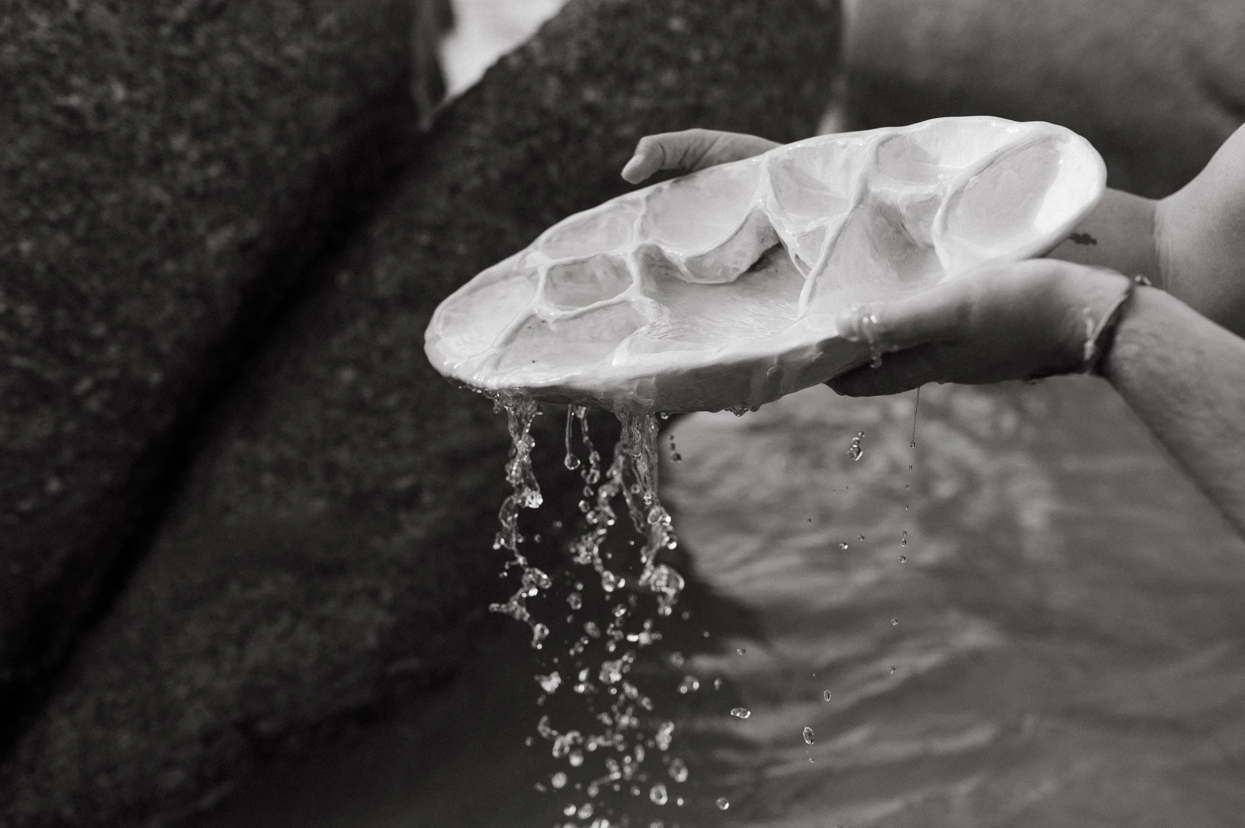 Hand holding a shallow dish with water overflowing, with water dripping from the edges, against a dark background.