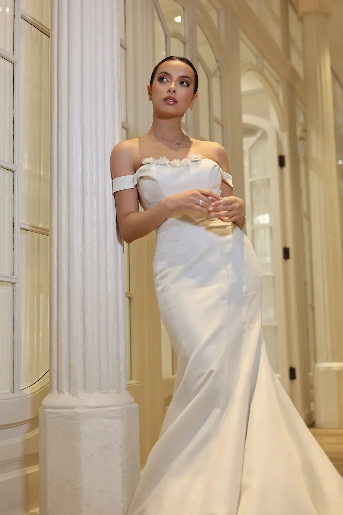 Clean look para novia, maquillaje en tonos suaves y recogido bajo. Novia de Pie sobre una columna blanca del Hotel en barcelona