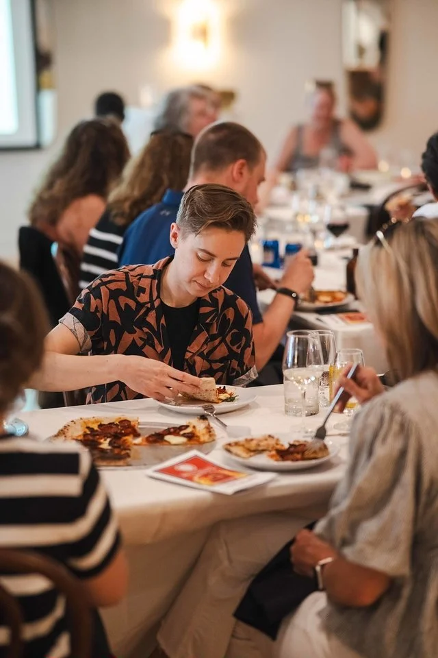 People dining at a restaurant table with pizza and drinks, engaged in conversation.
