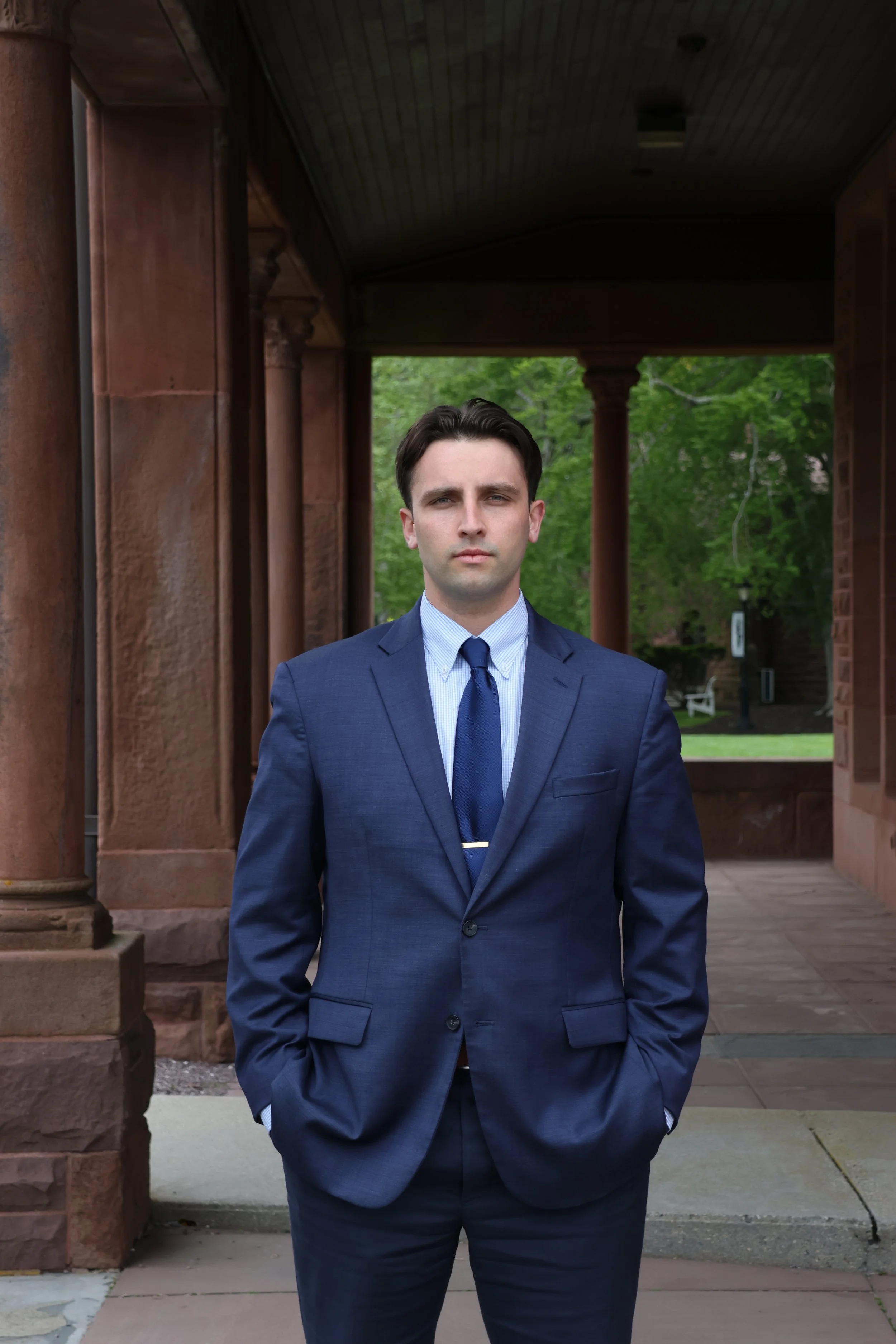 A young man in a blue suit and tie standing outside near a historic stone building with columns.