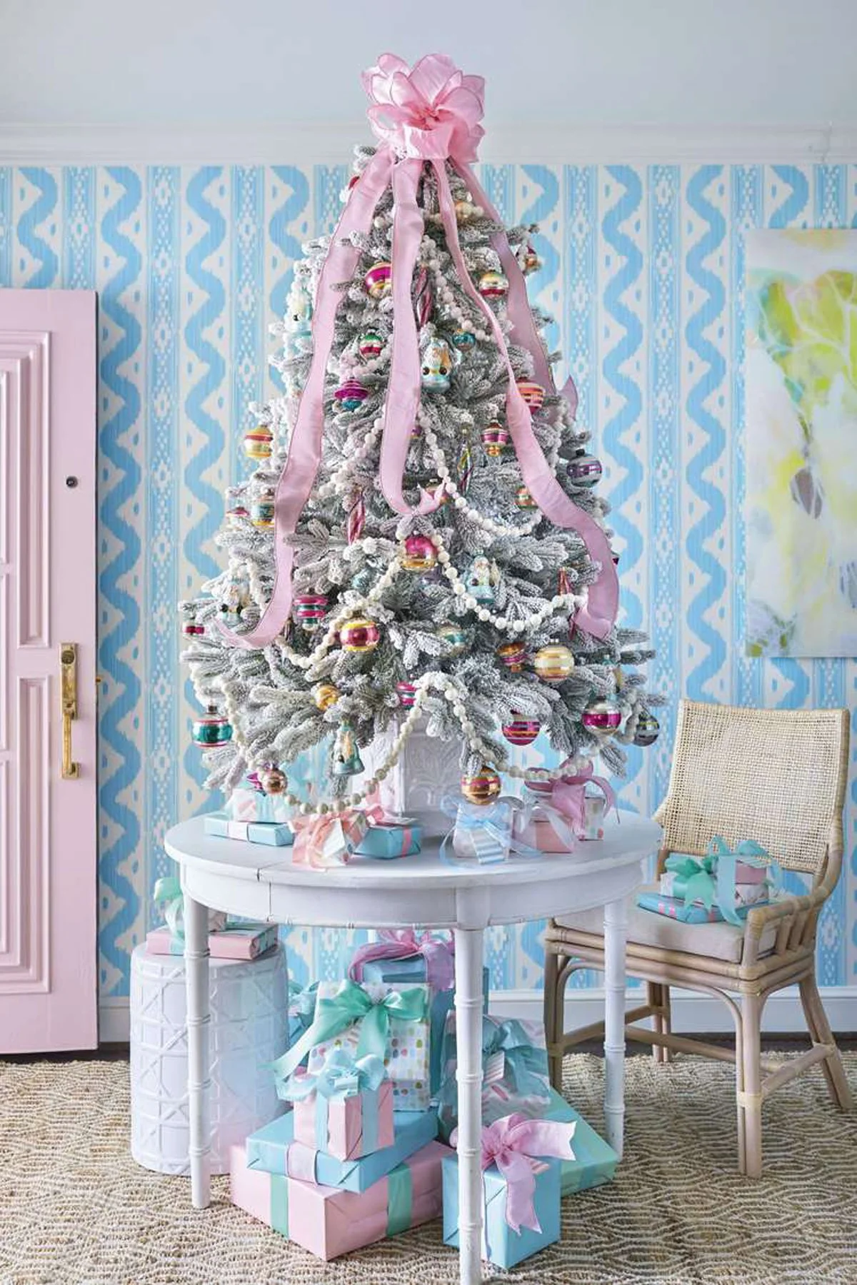 a frosted christmas tree covered in pink ribbon and pastel ornaments in a sky blue wallpapered room styled by lindsey ellis beatty