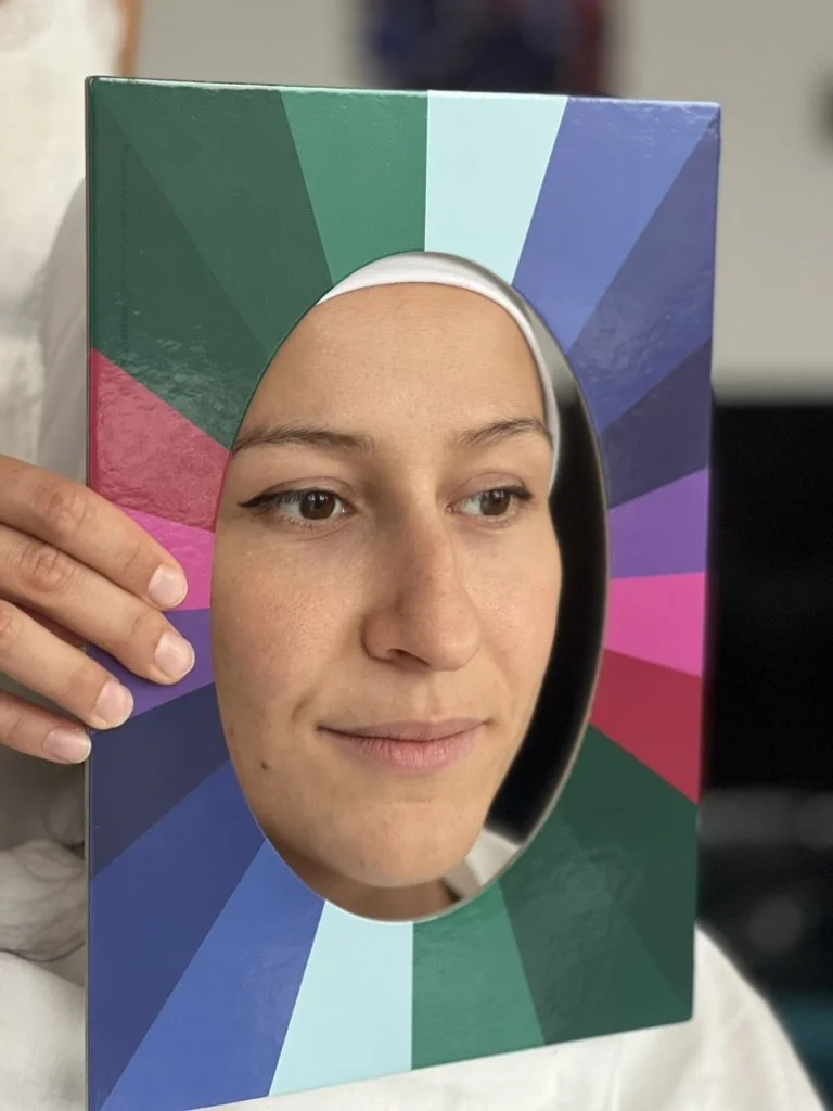 Person with face in color test chart for color analysis, holding a rainbow-colored frame.