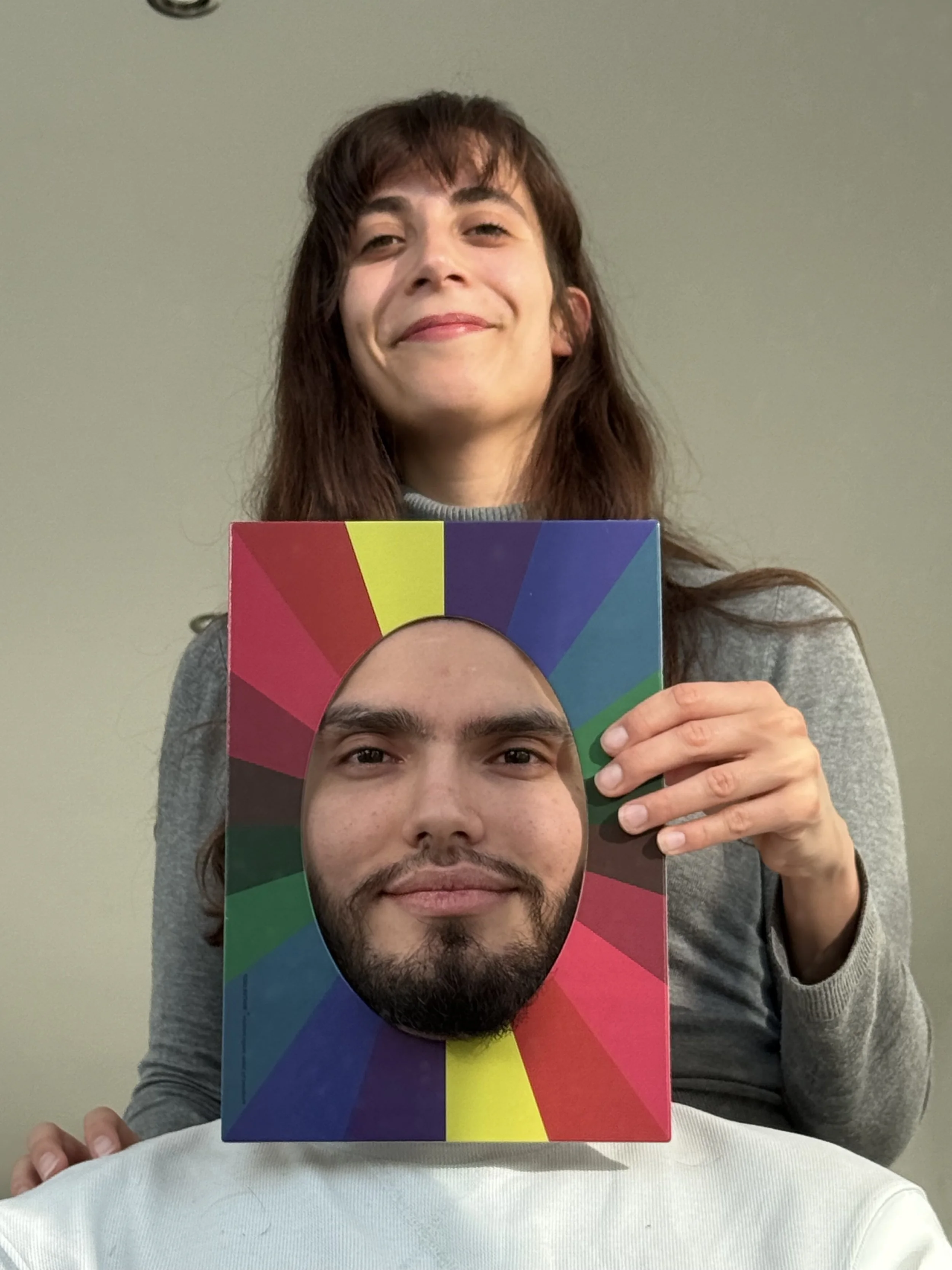 Woman holding a colorful board with a man's face cutout in the center.