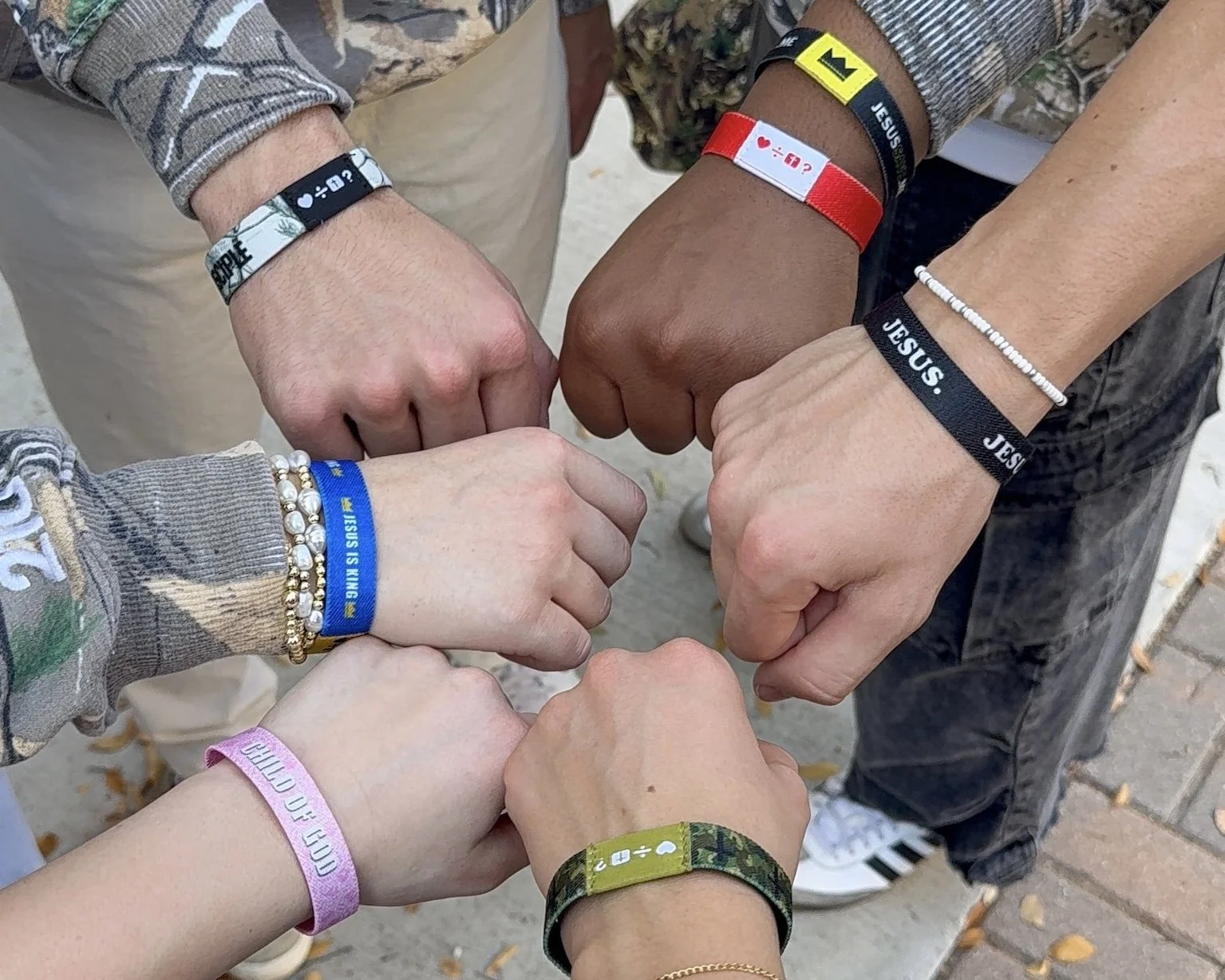 Stack of books with yellow and black covers, lanyards with religious symbols, and bracelets reading 'JESUS SAVE' on a light wooden surface. Emojivangelism keychains