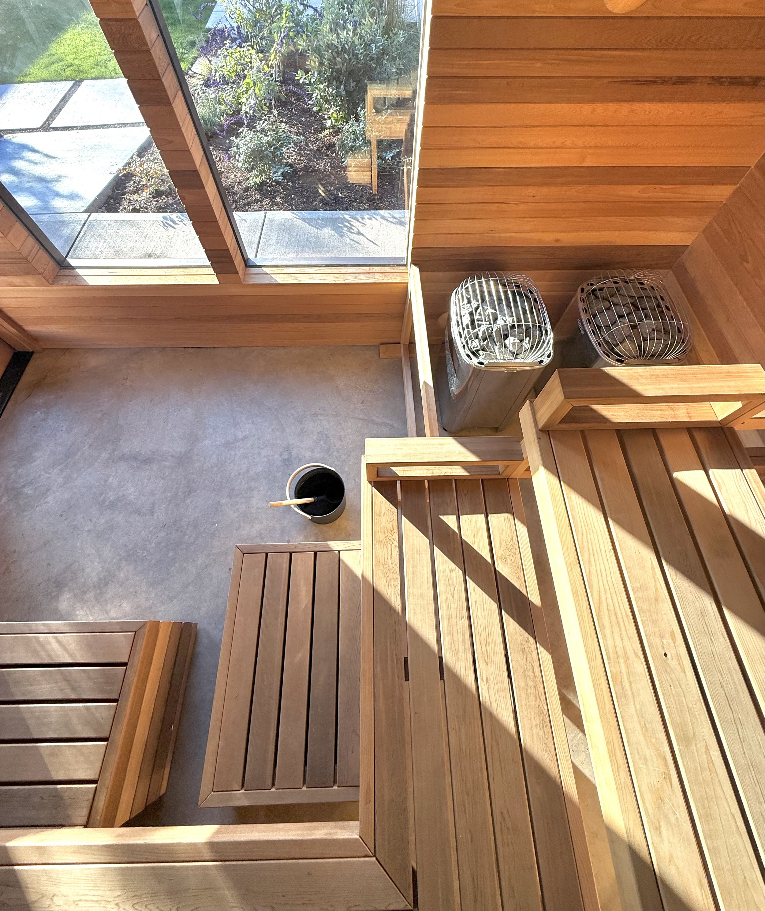 An interior of a wooden sauna with tiered benches and a bucket with a ladle on the floor.
