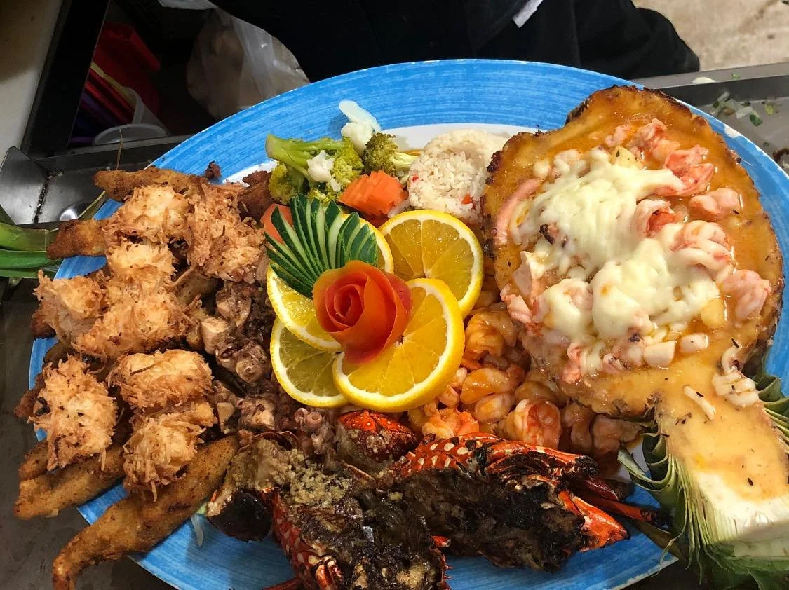 Seafood platter with fried shrimp, grilled lobster tail, baked seafood dish, lemon slices, and vegetables on a large blue plate.