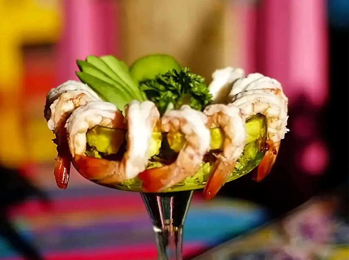 Seafood cocktail served in a glass with shrimp, avocado slices, cucumber, and parsley garnish.