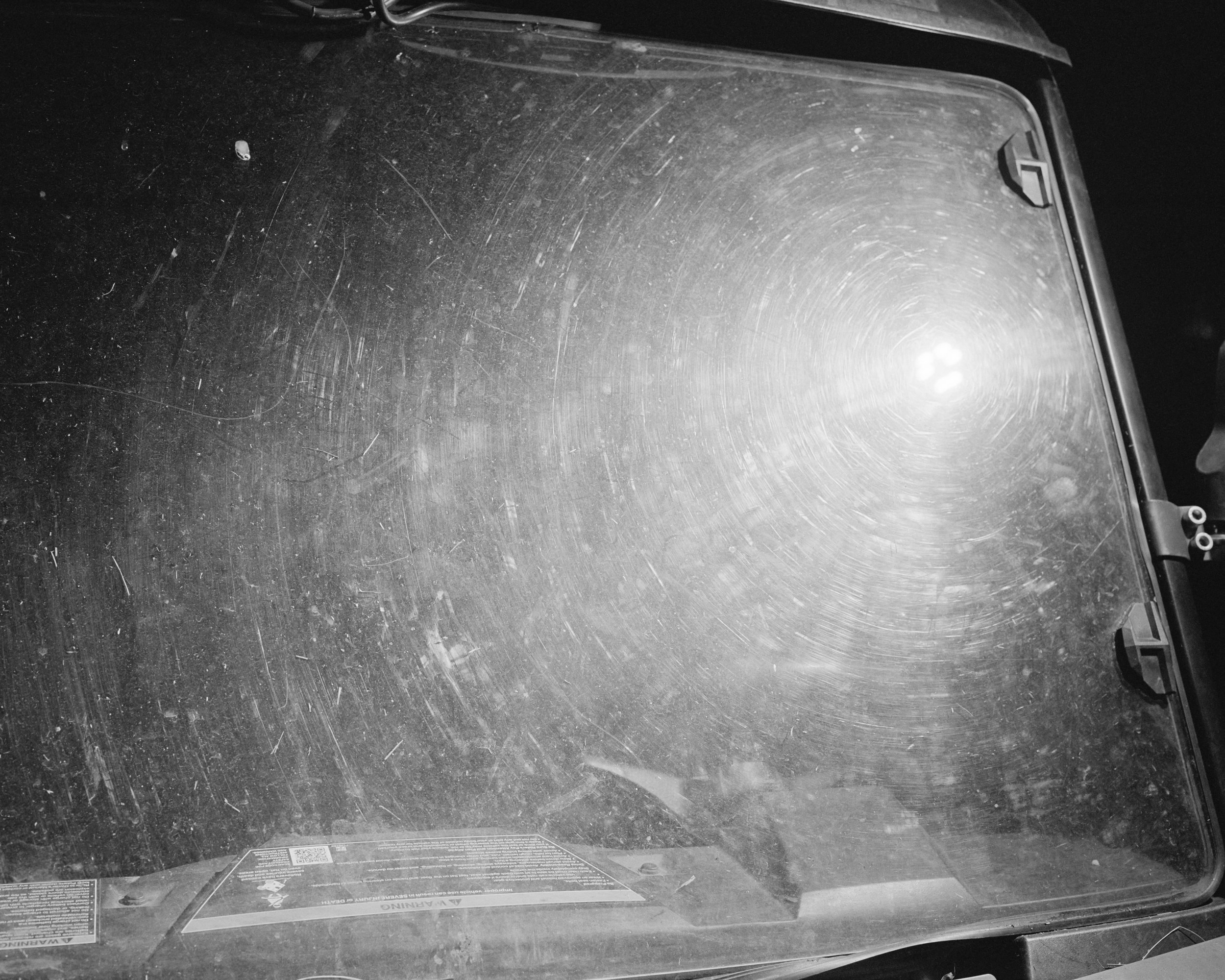 Black and white image of a flashlight glare on a scratched windshield.