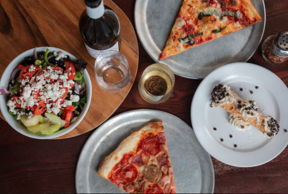 Pizza slices, salad, bottled drink, water glass, and a dessert on a wooden table.
