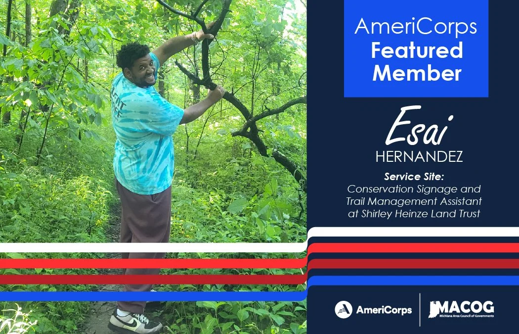 Esai standing on a trail in the woods holding up a large tree branch that fell.