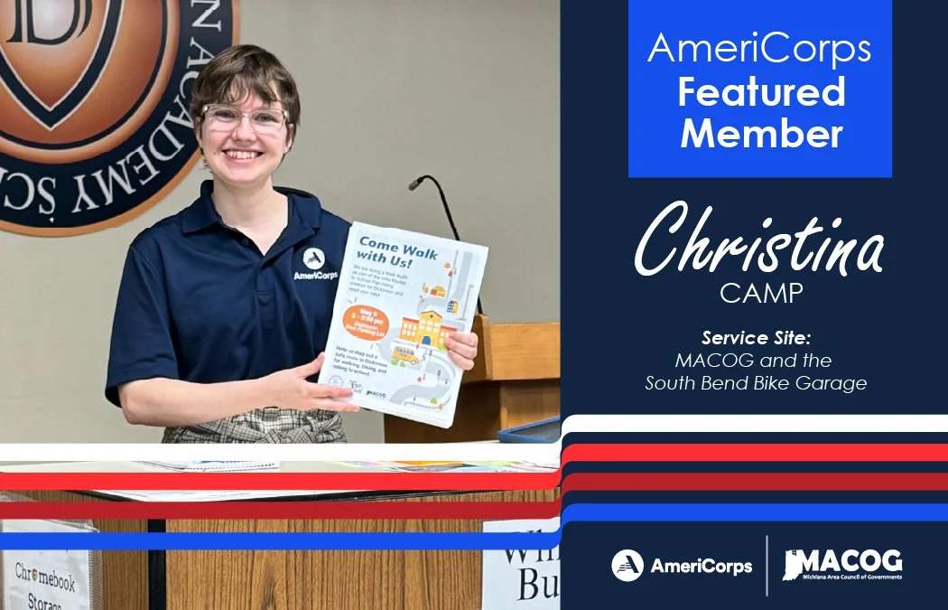 Christina is smiling, standing behind a podium wearing an AmeriCorps dark blue polo, holding up a flyer promoting an event.