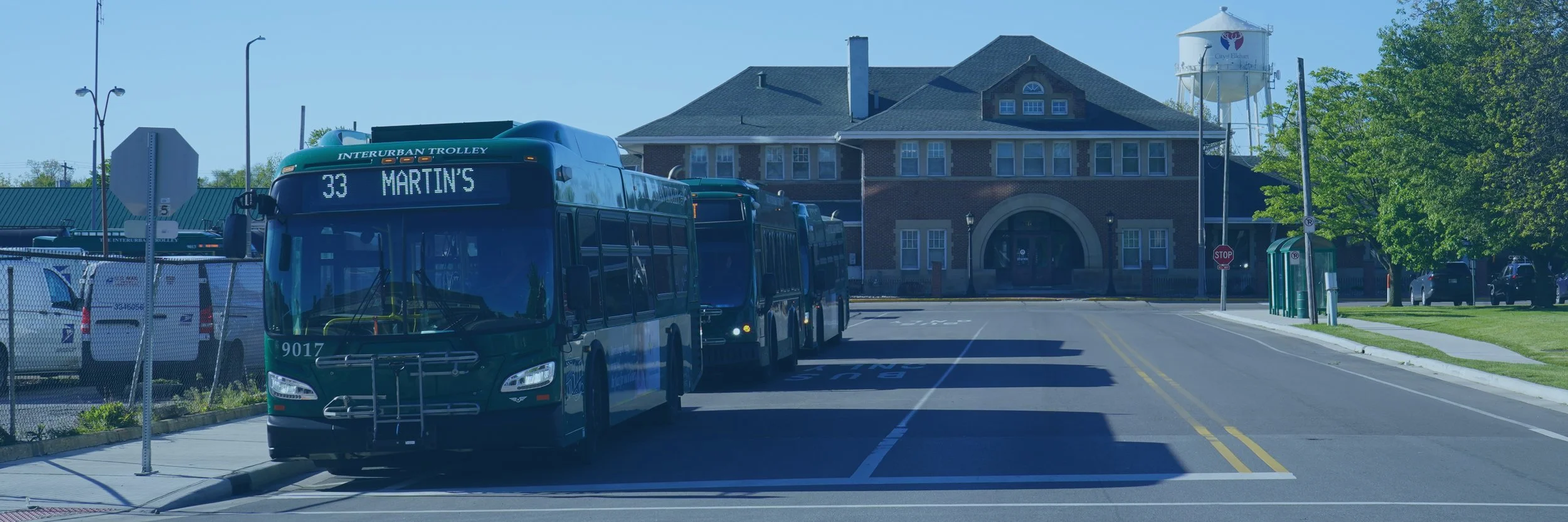 Three Trolley buses in line at the Elkhart Transfer Center with the Amtrak station seen behind